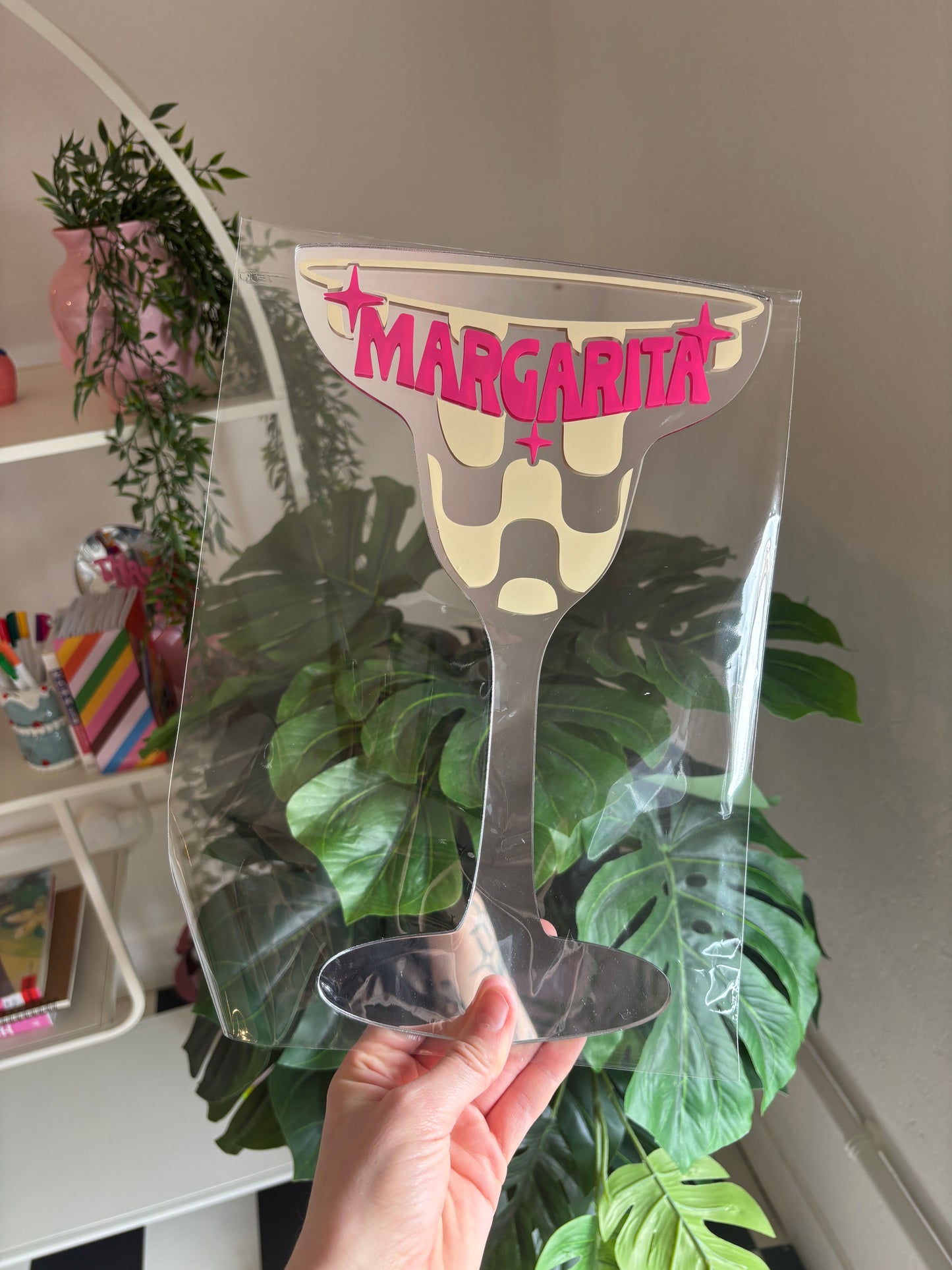 A hand is holding a clear plastic margarita glass with the word "MARGARITA" written on it.