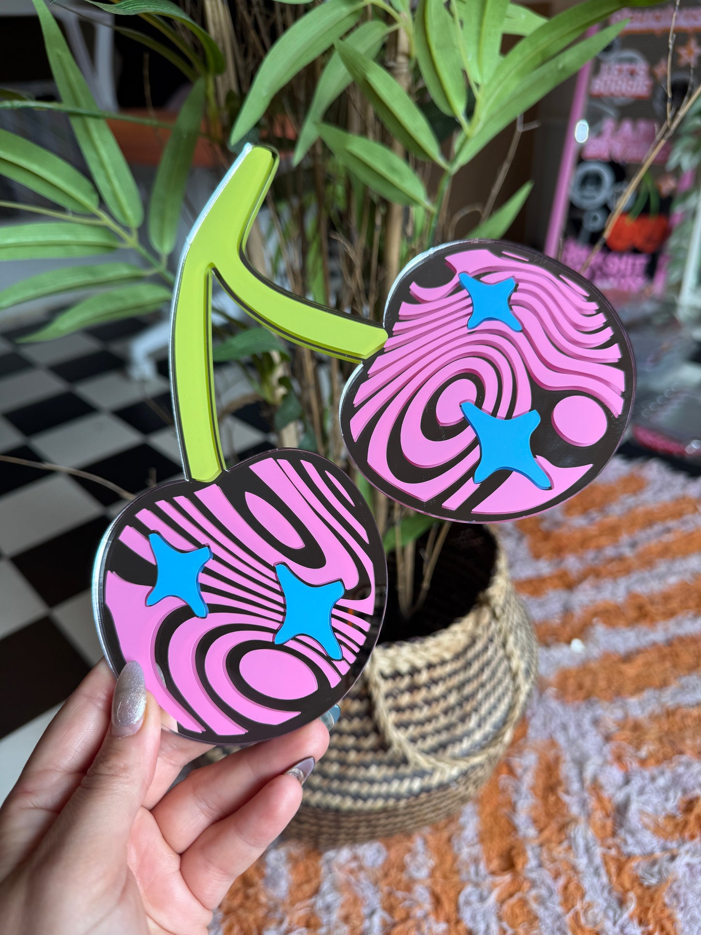 A hand is holding a pair of colorful, abstract, and stylized coaster-like objects with a mix of pink, blue, and black designs.