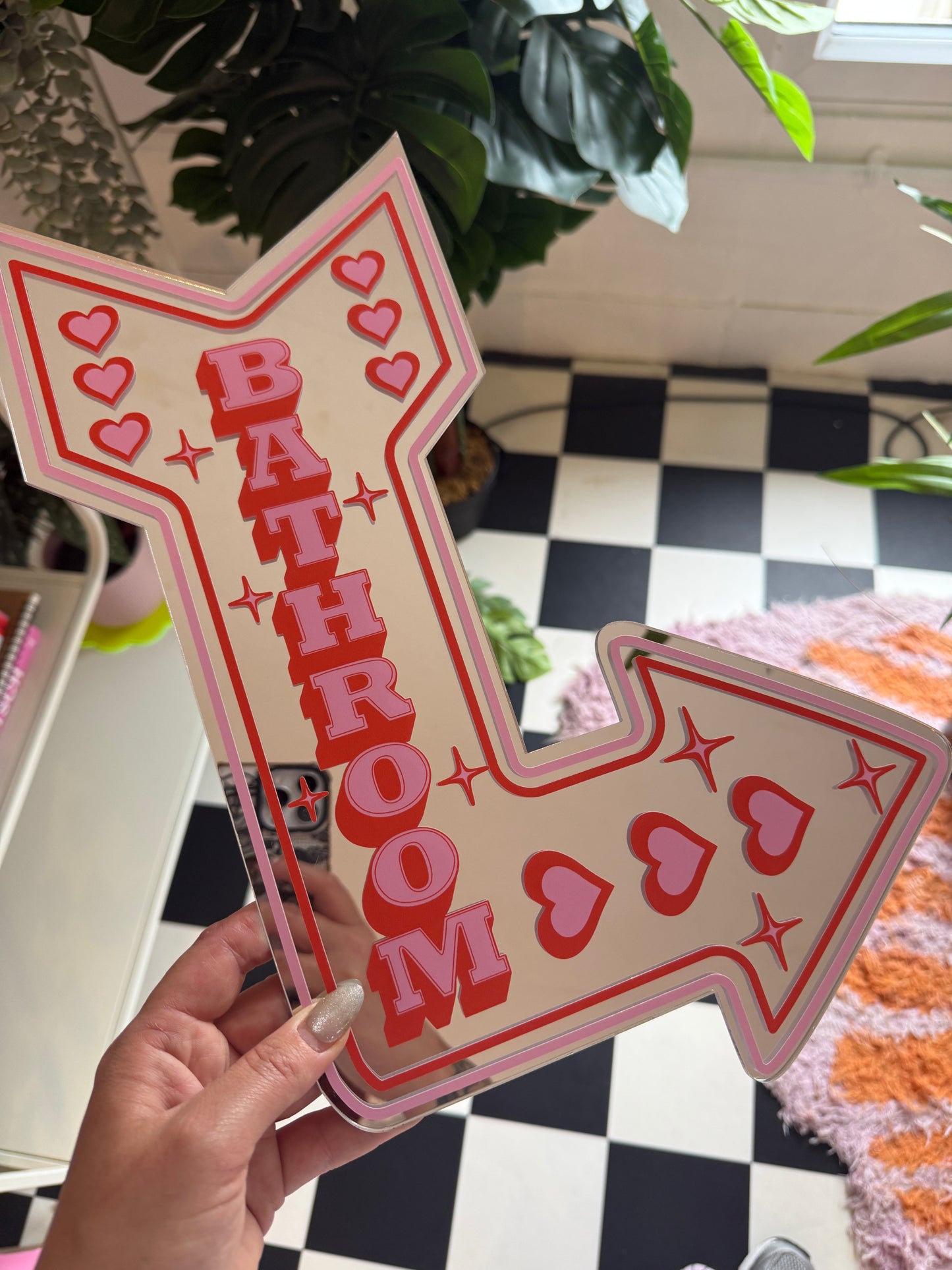 A hand is holding a pink arrow-shaped sign with the word "BATHROOM" written on it.
