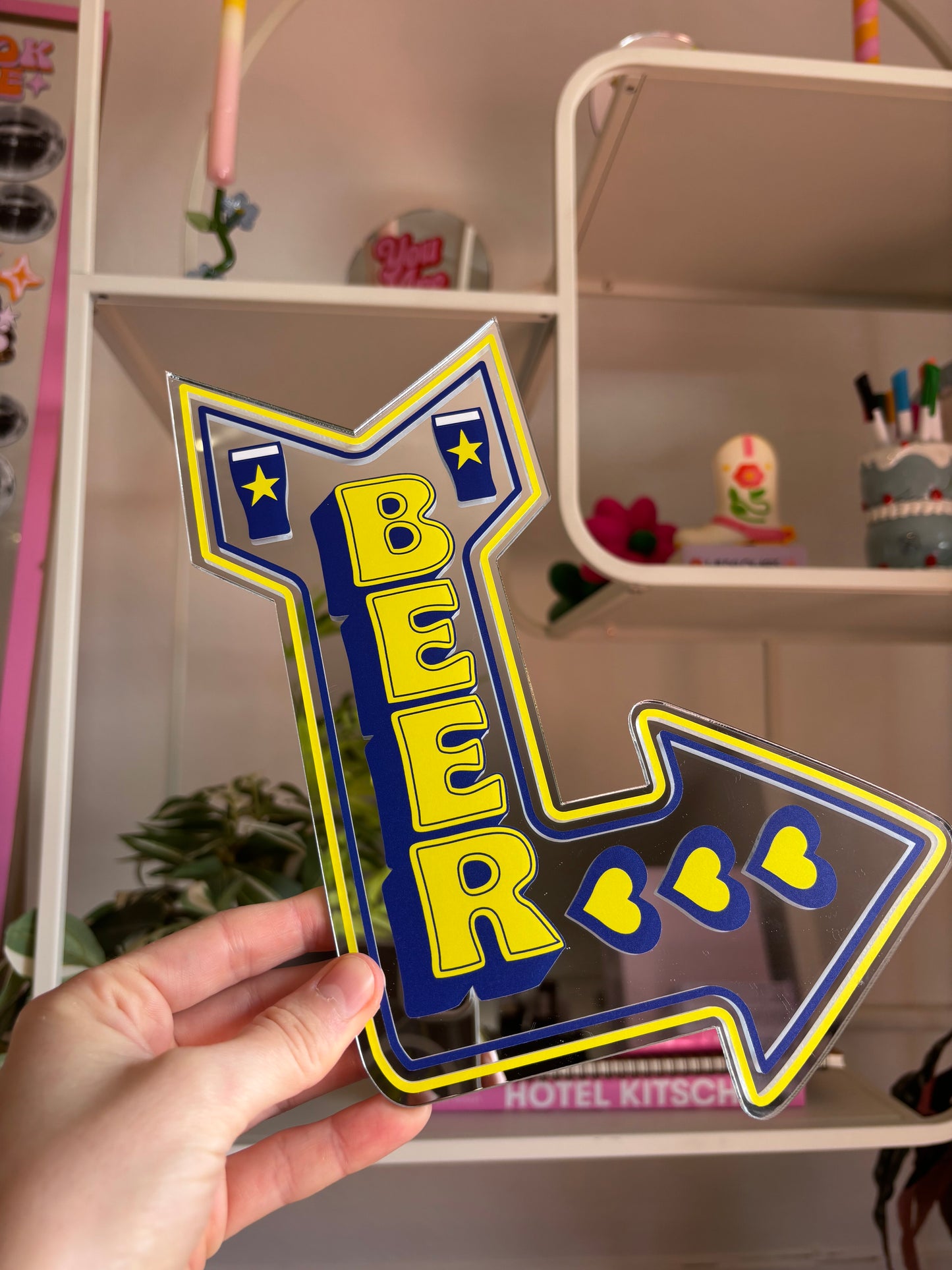 A hand is holding a sign that says "BEER" in yellow and blue colors, with a heart symbol between the letters.