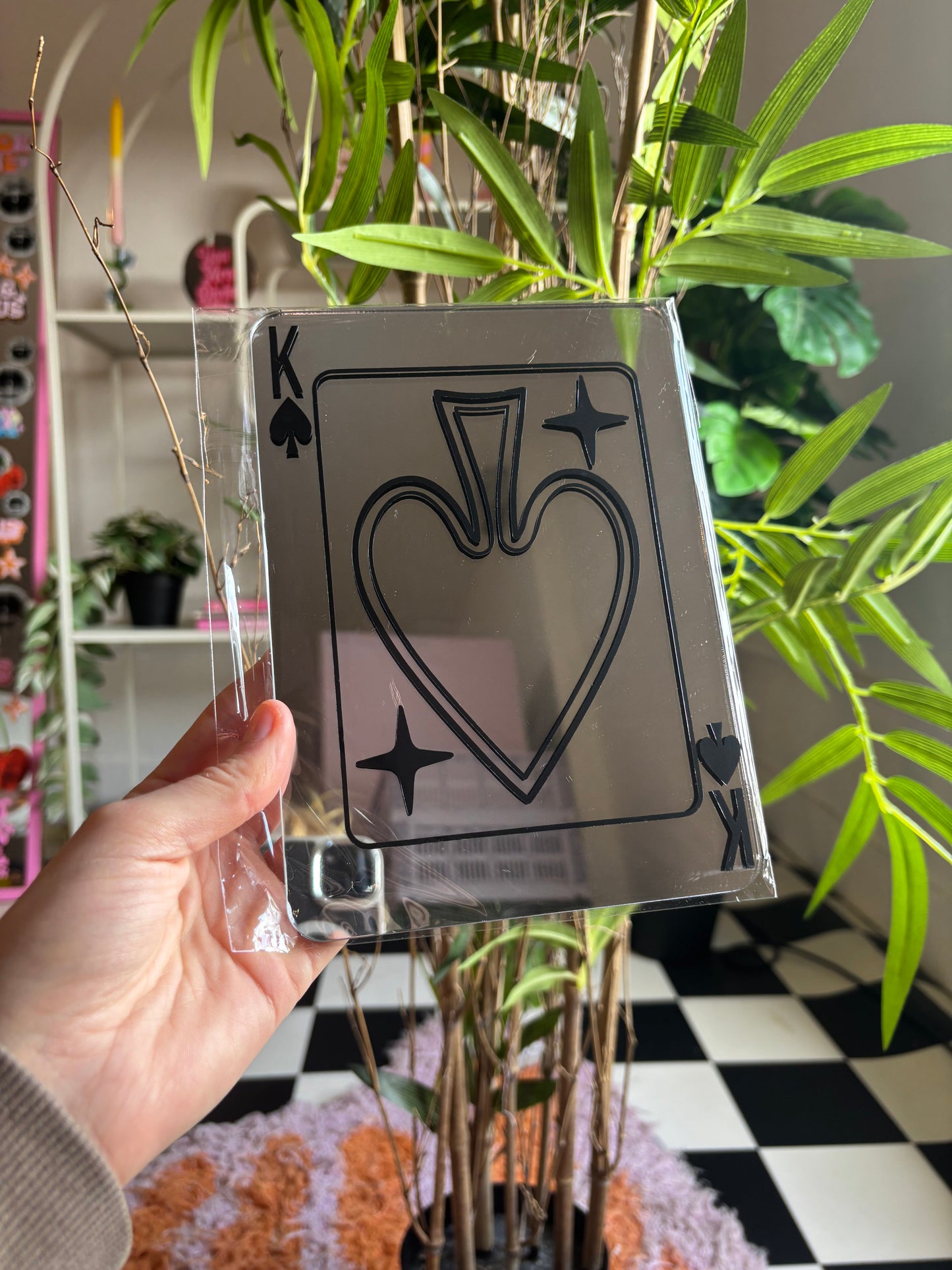 A hand is holding a transparent card with a black playing card design on it, which appears to be a koker or king of spades.