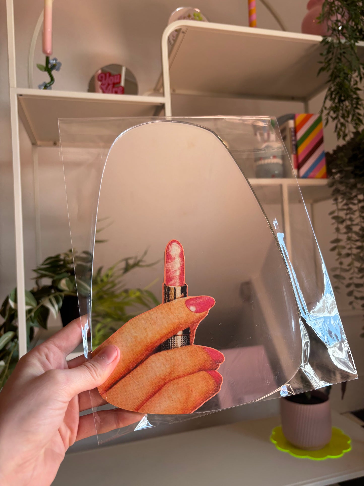A hand is holding a clear plastic sheet with a hand holding a red lipstick image on it.