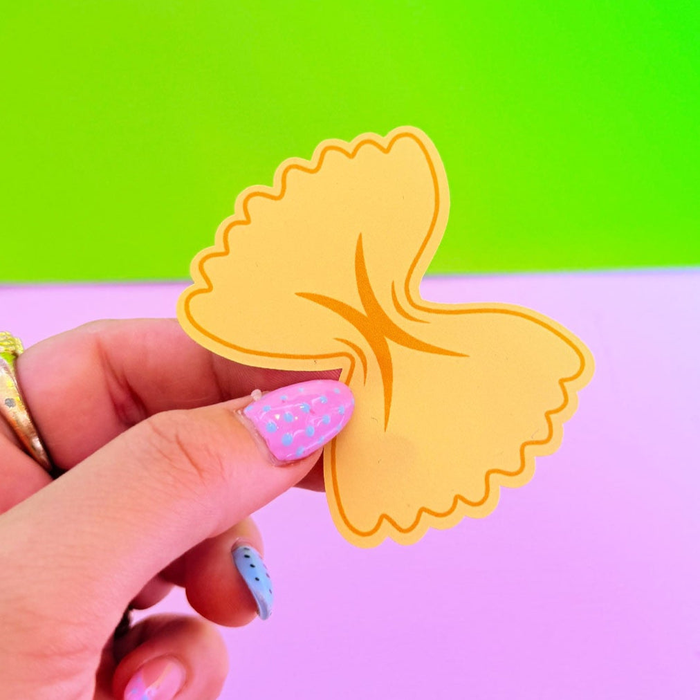 Hand holding a yellow pasta shape against a gradient background