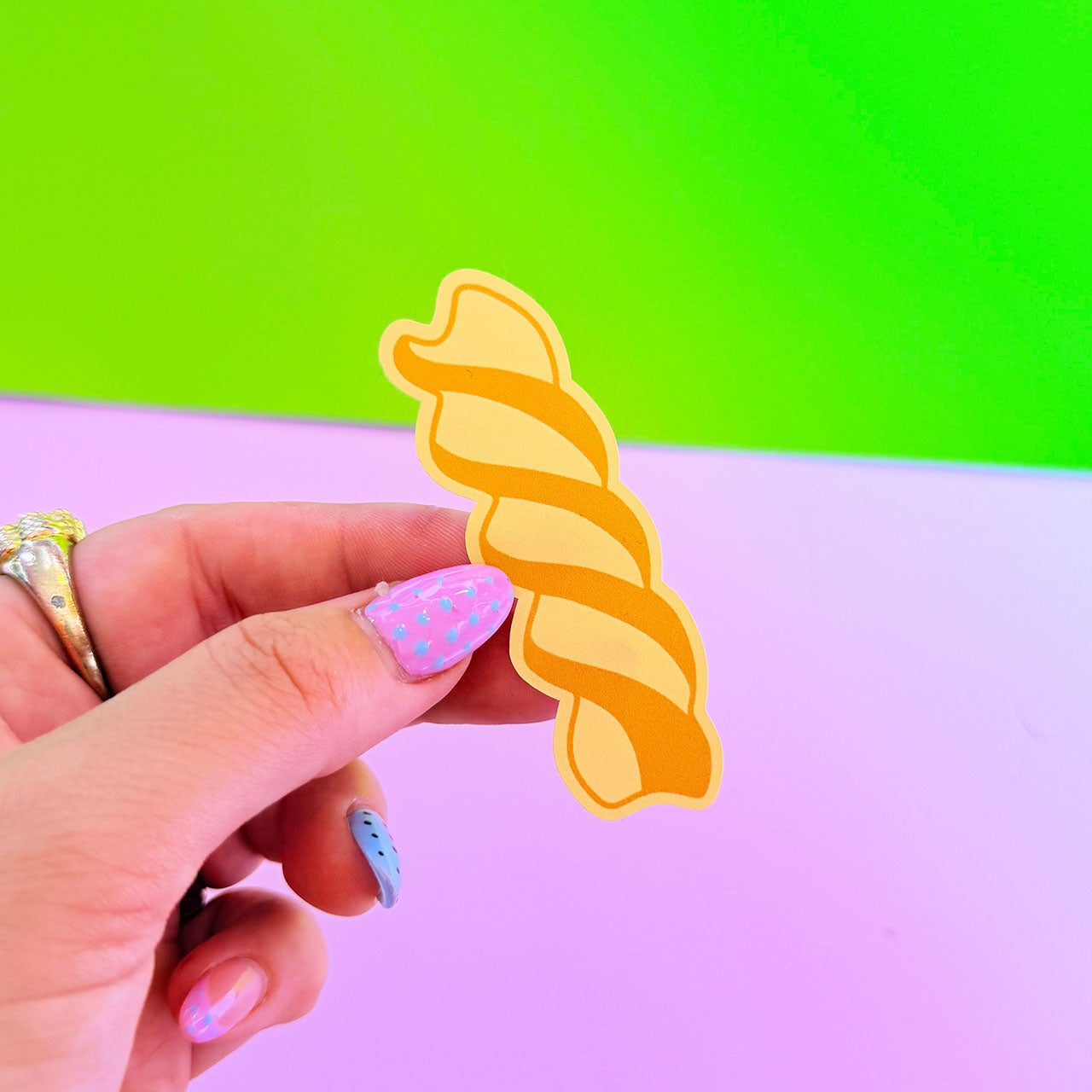 Hand holding a yellow spiral pastaagainst a green and pink gradient background