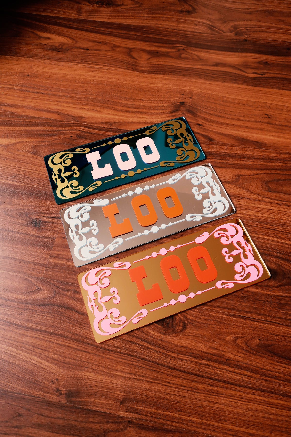 three colorful license plates with the word "LOO" written on them, arranged on a wooden surface.