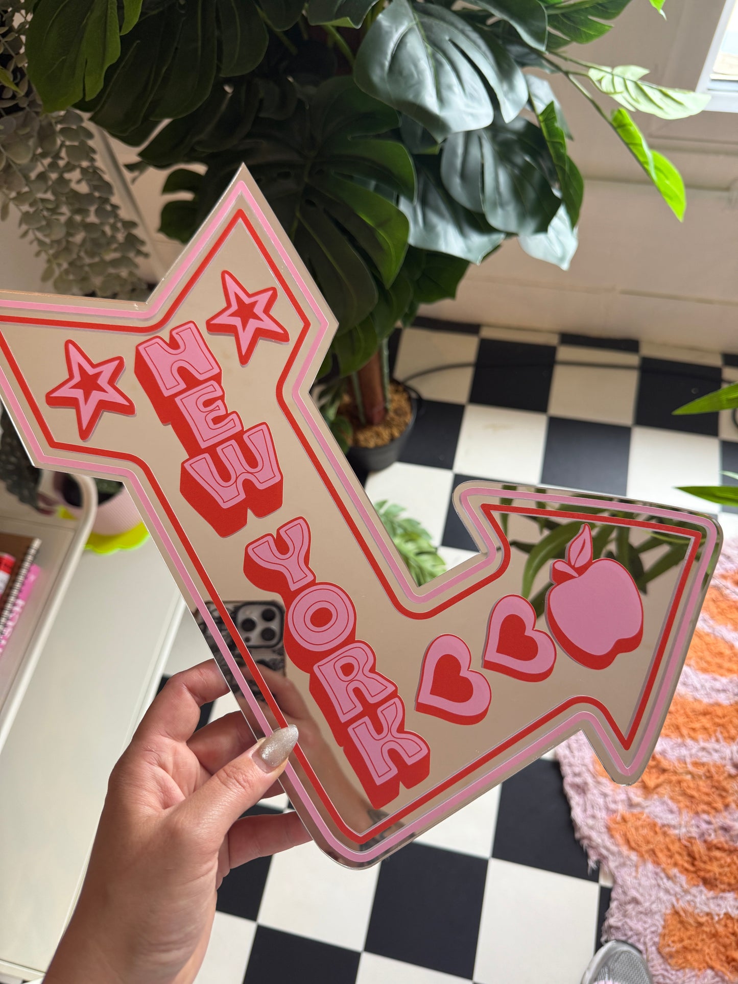 A hand is holding a pink arrow-shaped sign with the text "ZUH" on it, which appears to be a stylized version of the word "ZUH" in a pink and red color scheme.