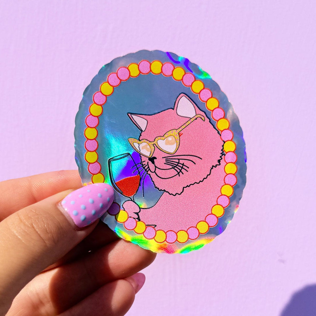 Hand holding a colorful sticker with a cat design against a purple background