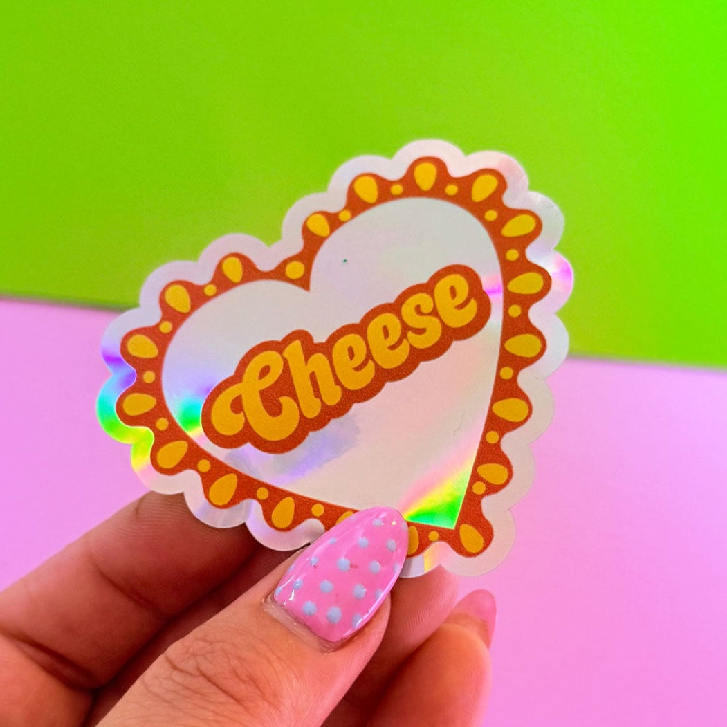Hand holding a colorful 'Cheese' sticker against a green and pink background