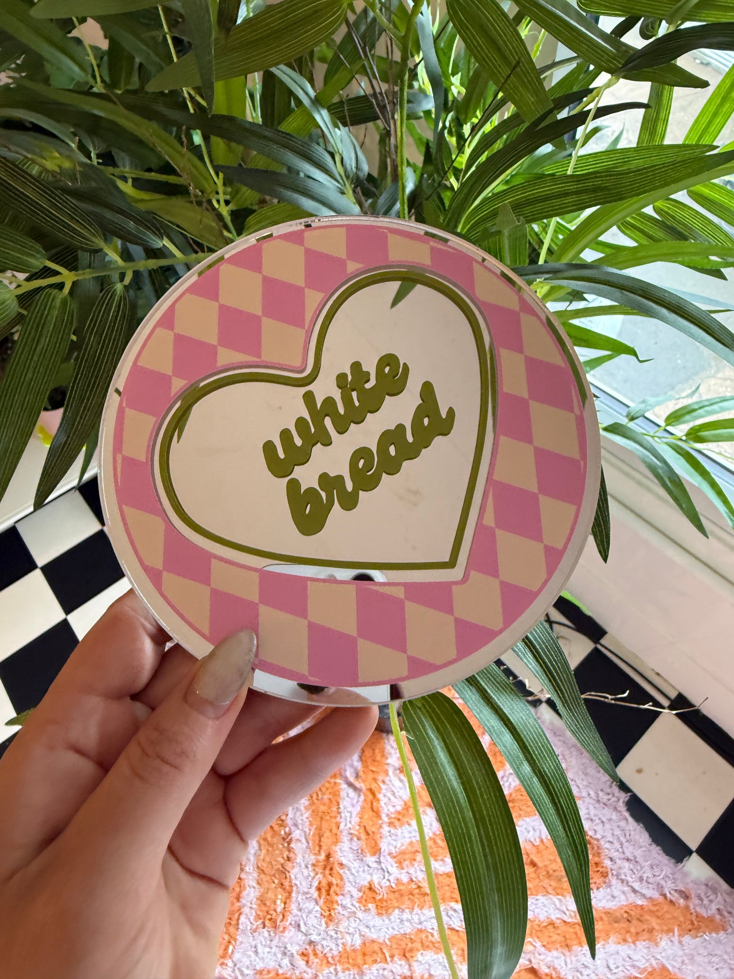 A hand holding a heart-shaped sticker with the text "While I was in the mood for some ice cream" printed on it, surrounded by green leaves and a checkered pattern.