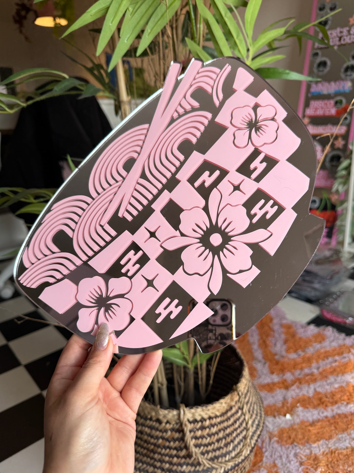 A hand is holding a decorative object with a floral pattern in pink and black colors.