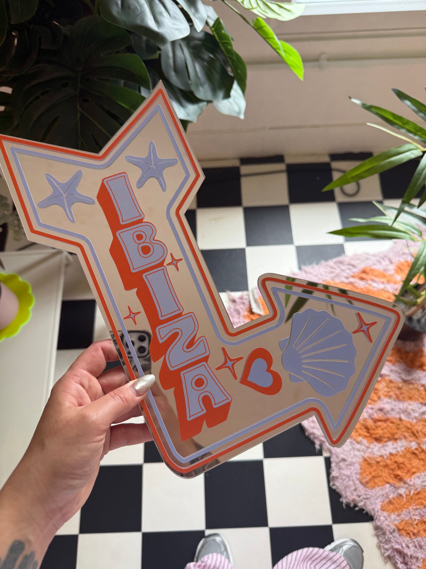 A hand holding a large, colorful sign with various decorative elements such as a shell, star, and heart.