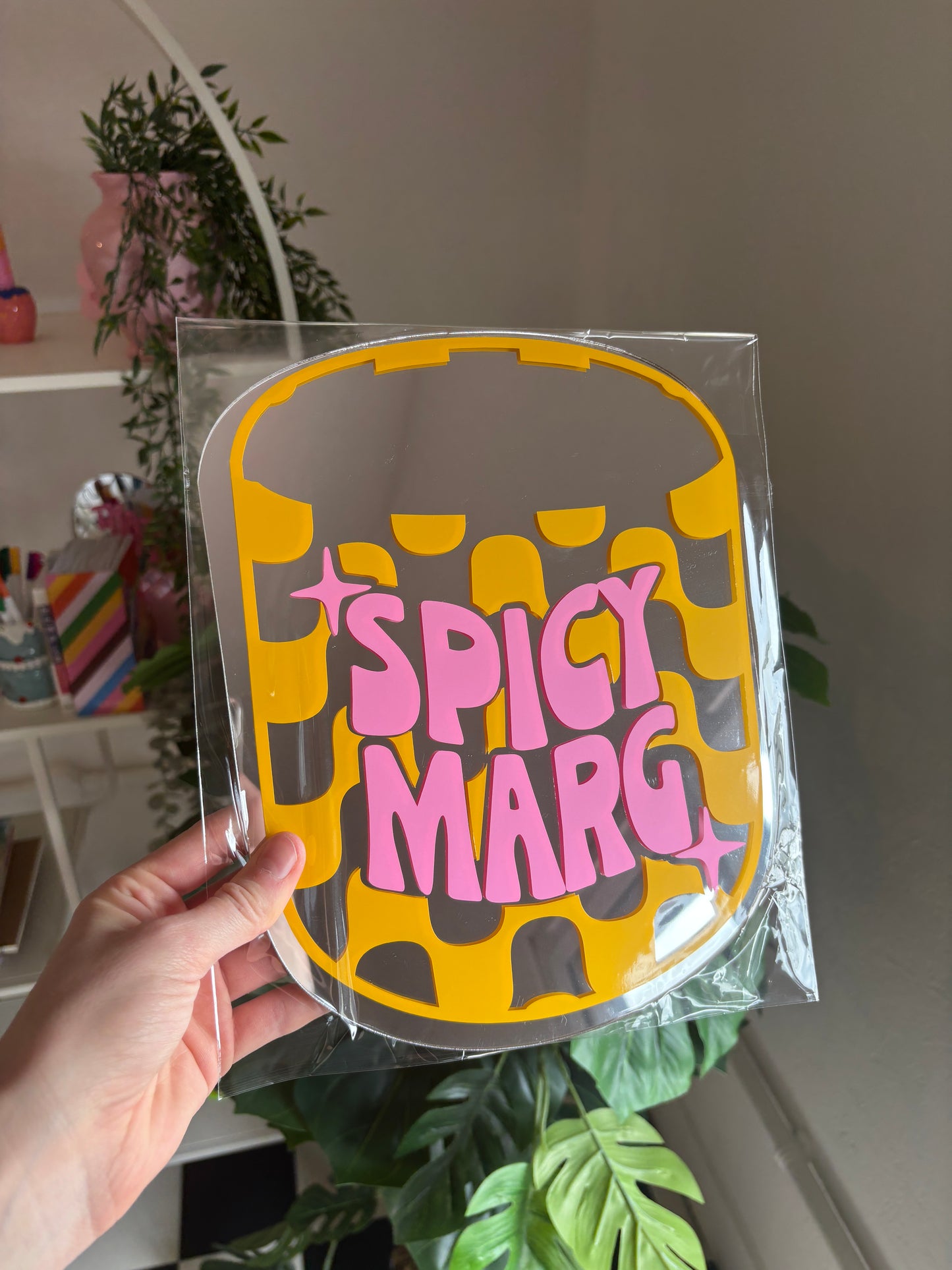 A hand is holding a yellow and pink sign with the text "SPICY MARG" on it.