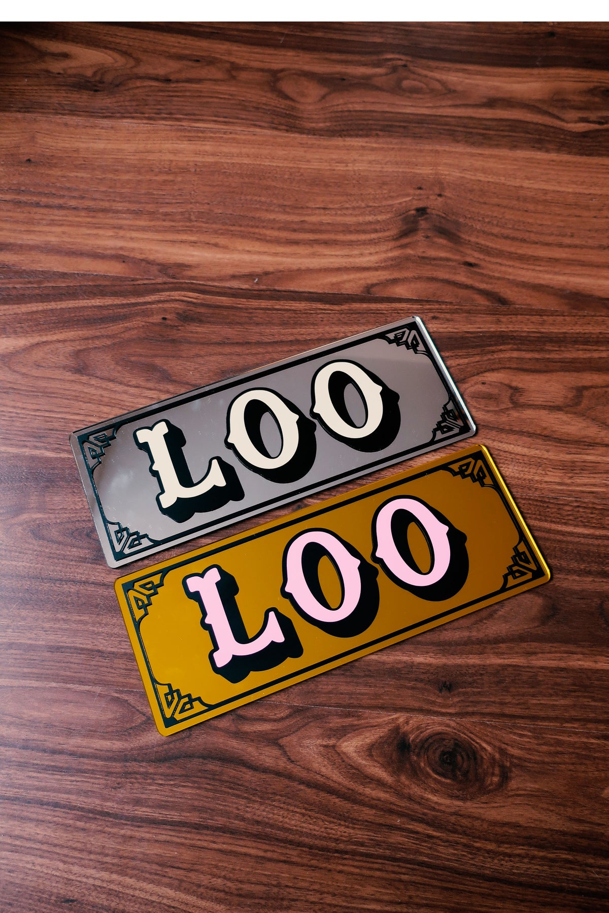 two rectangular signs with the word "LOO" written on them, placed on a wooden surface.