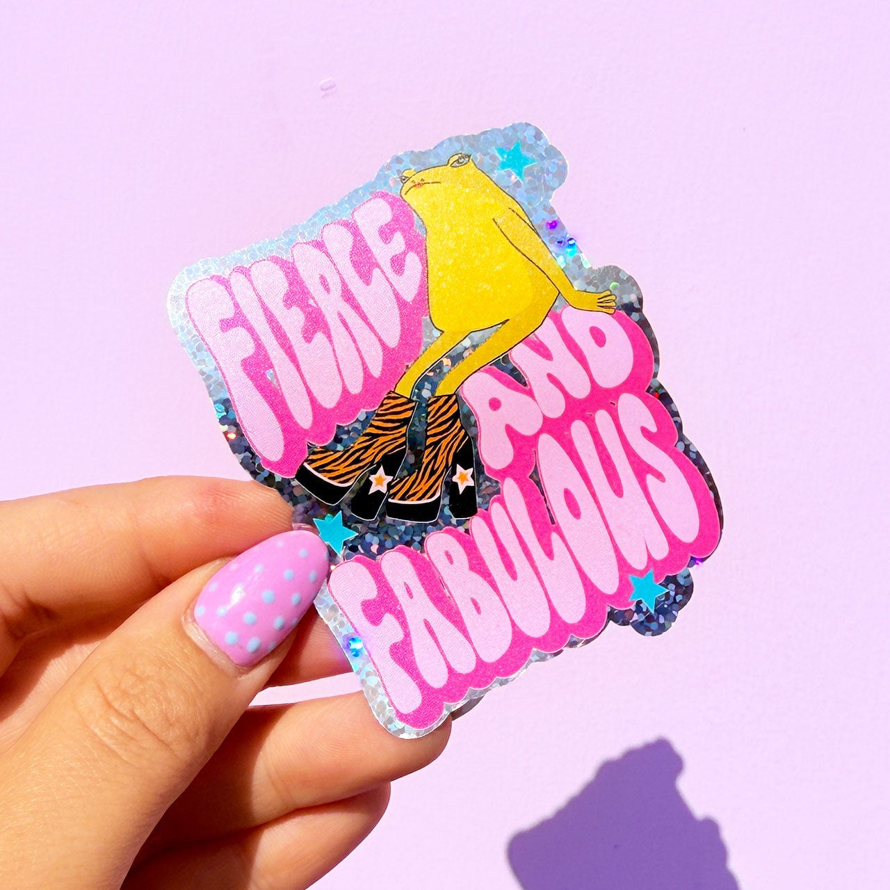 Sticker with 'Fierce Loud Fabulous' text held by a hand on a purple background