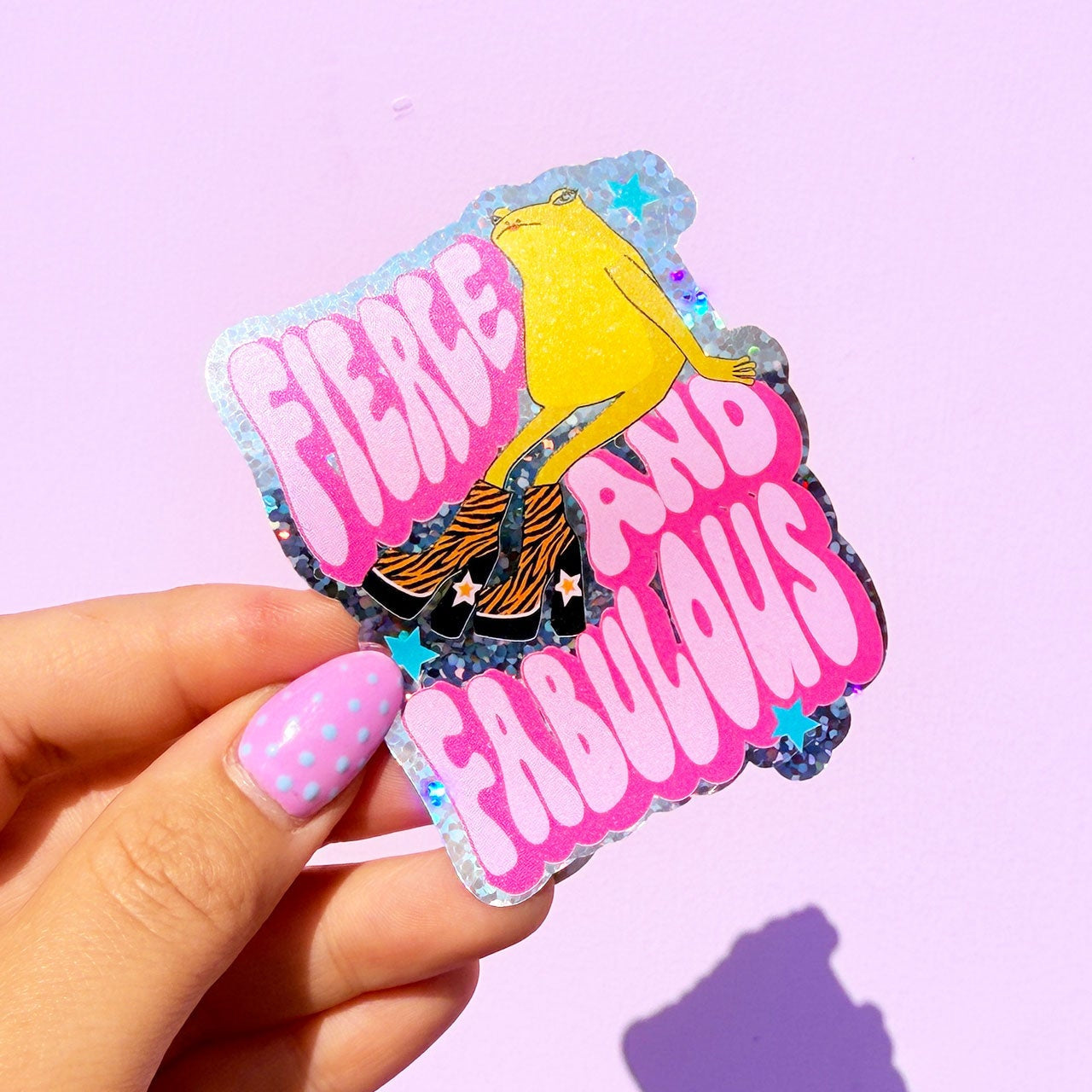 Sticker with 'Fierce Loud Fabulous' text held by a hand on a purple background