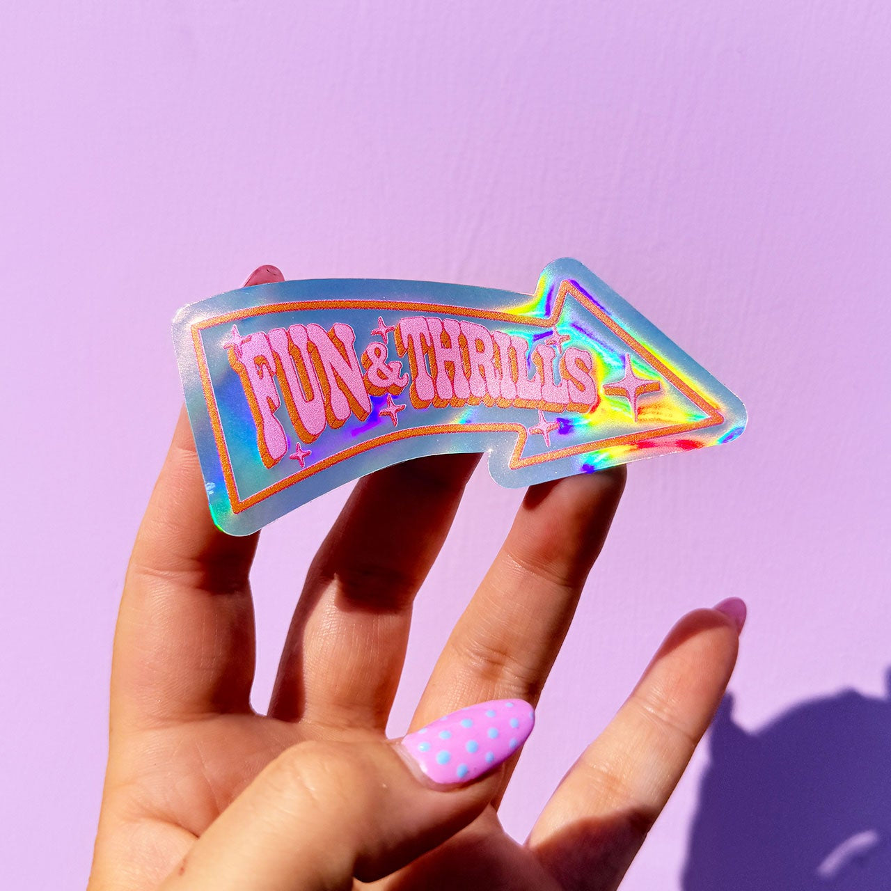 Hand holding a holographic 'Fun & Thrills' sign against a purple background
