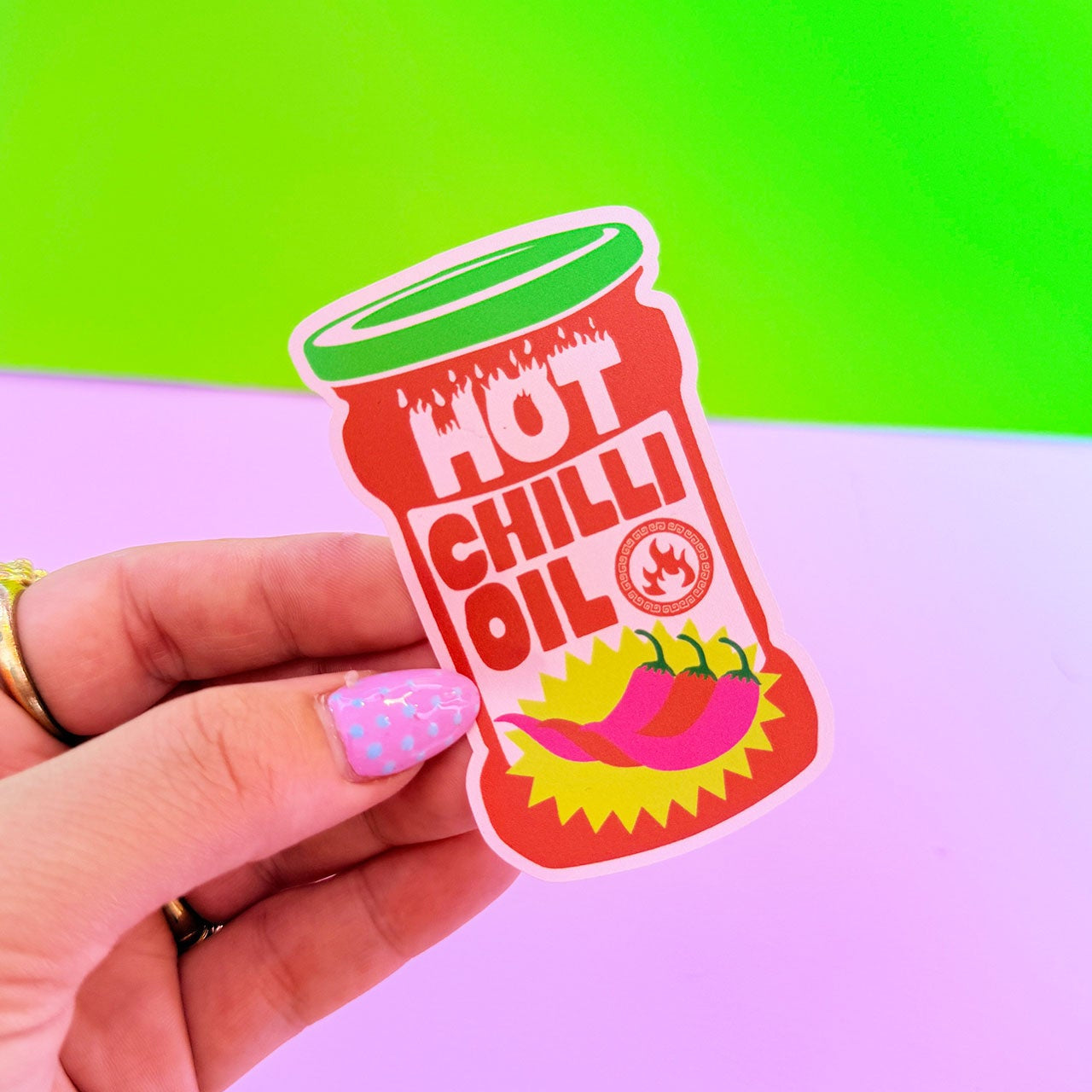 Sticker of a hot chili oil container held by a hand against a colorful background