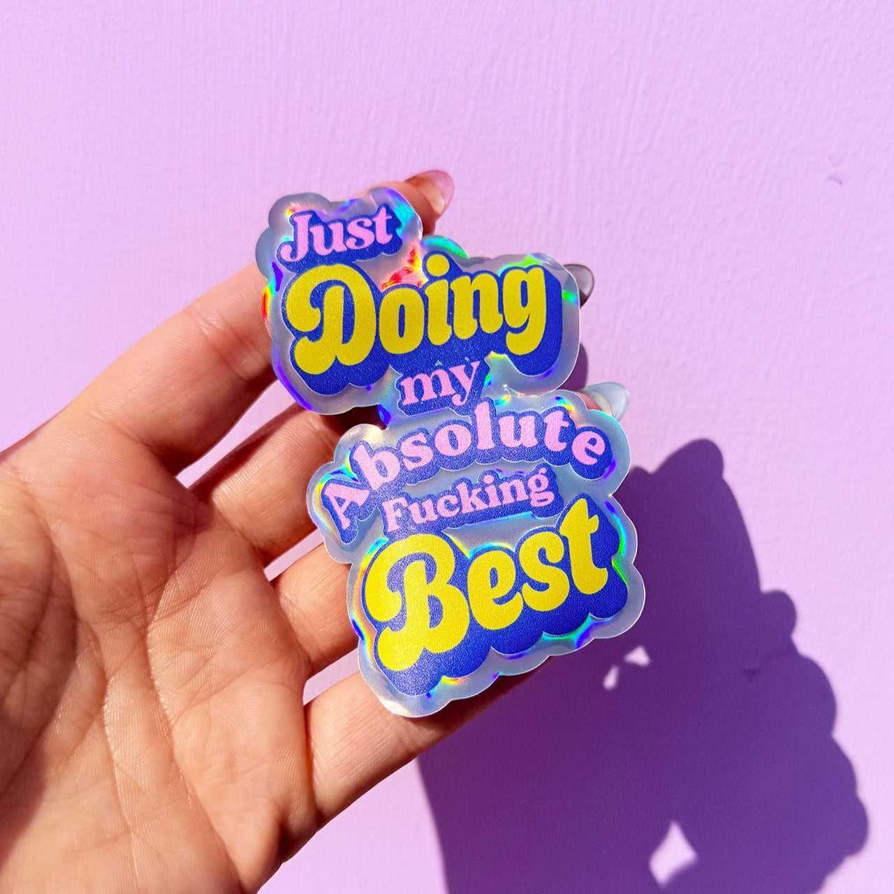 Hand holding a colorful sticker with motivational text against a purple background