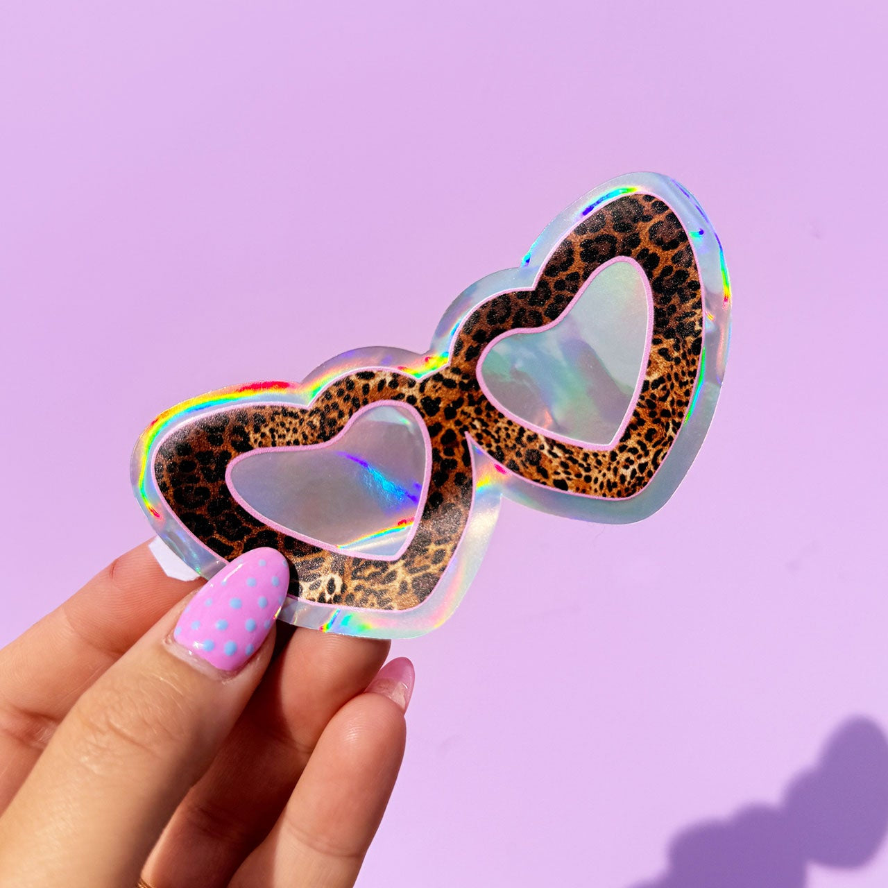 Holographic heart-shaped object with leopard print pattern held by a hand against a purple background