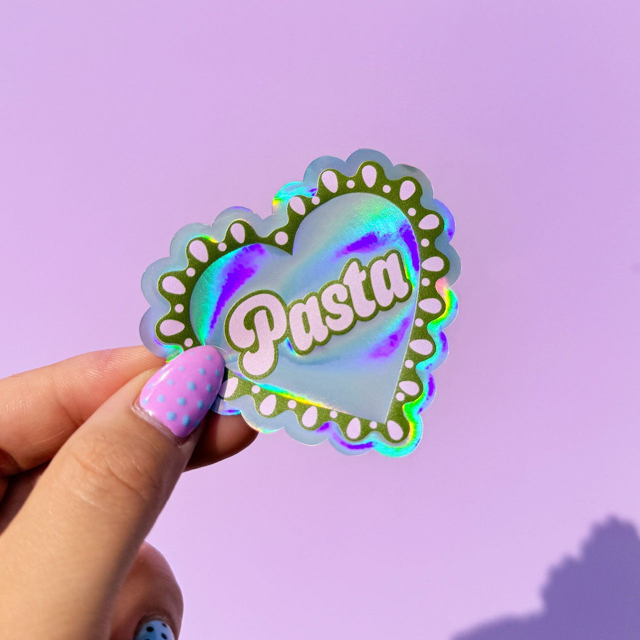 Hand holding a holographic 'Pasta' sticker against a purple background