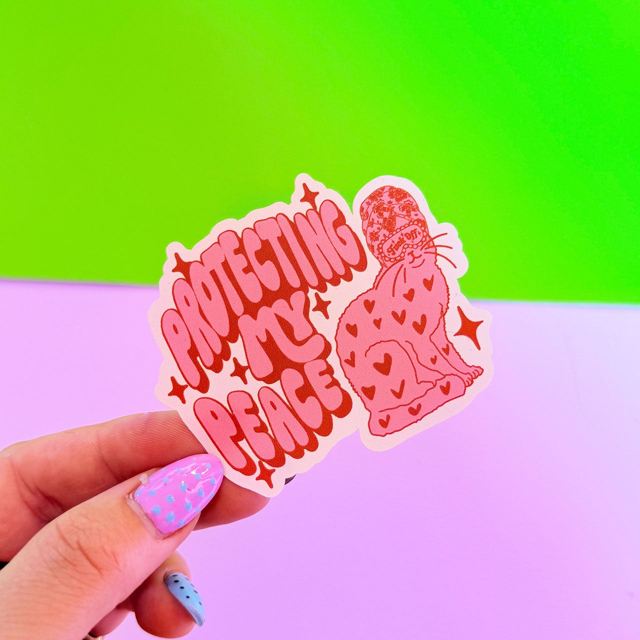 Hand holding a pink sticker with text against a green and purple gradient background