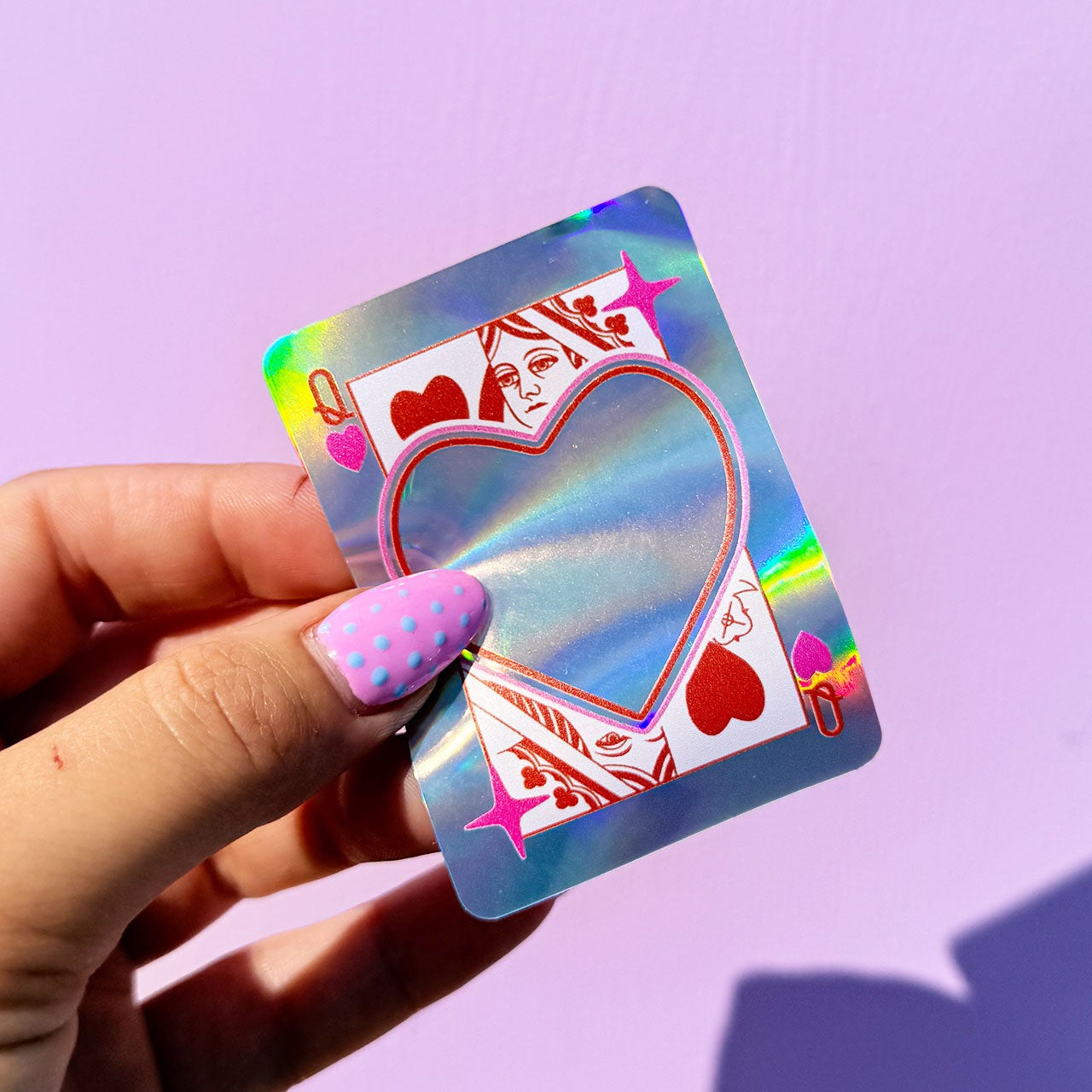 Hand holding a holographic card with a heart design against a purple background