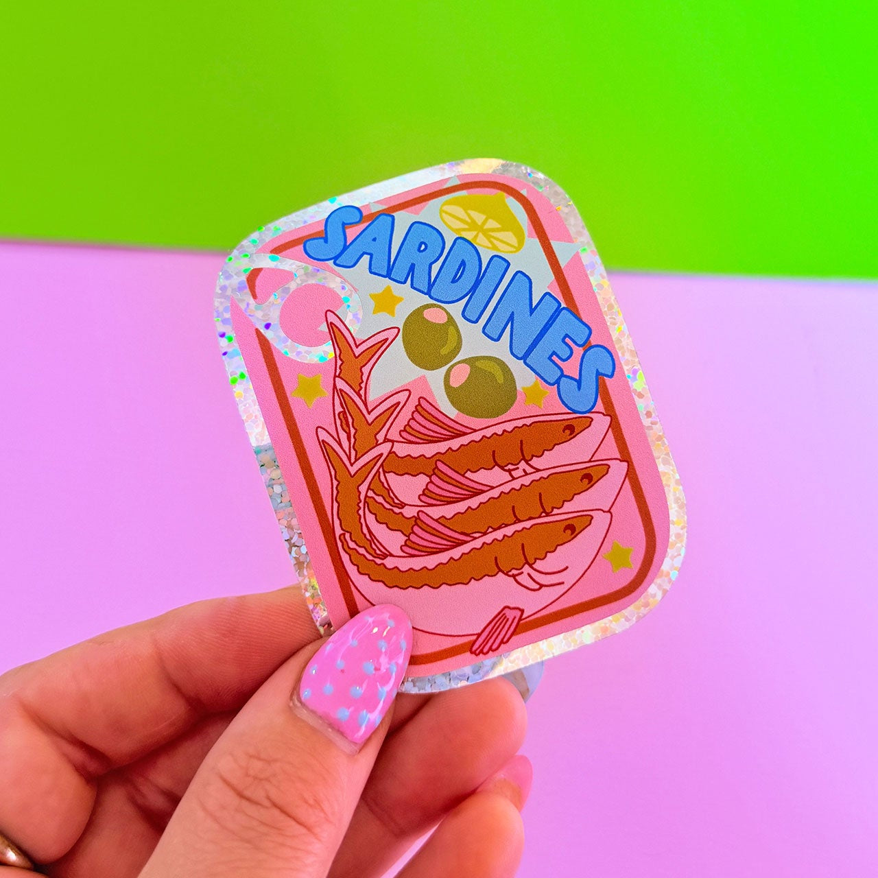 Colorful 'Sardine' sticker held by a hand against a green and pink gradient background