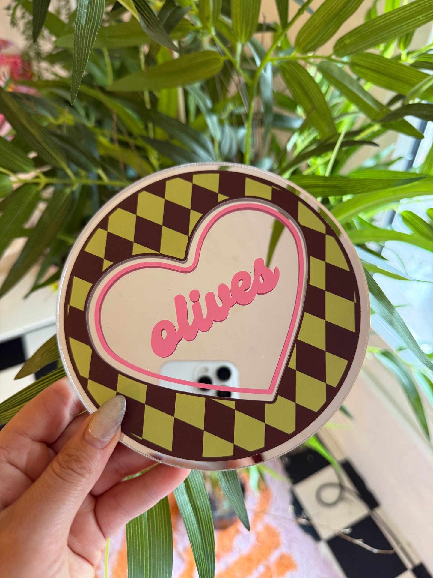 A hand holding a heart-shaped object with a checkered pattern and the word "Lucky" written on it, against a backdrop of green leaves and a checkered pattern.