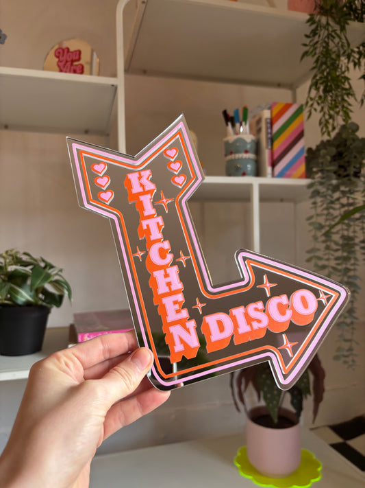 A hand is holding a large sign with the word "KITCHEN DISCO" written on it in a stylized font.