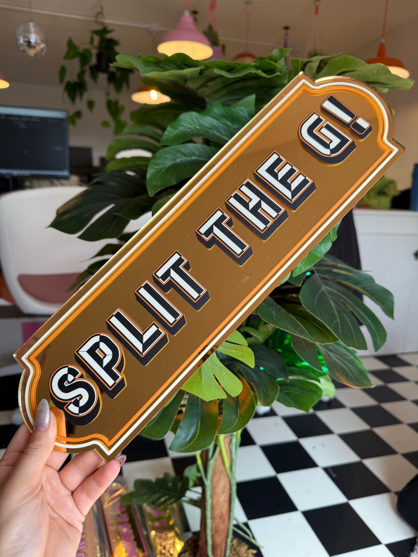 A person is holding a sign with the word "SPLIT" on it, surrounded by various plants and a checkered floor.