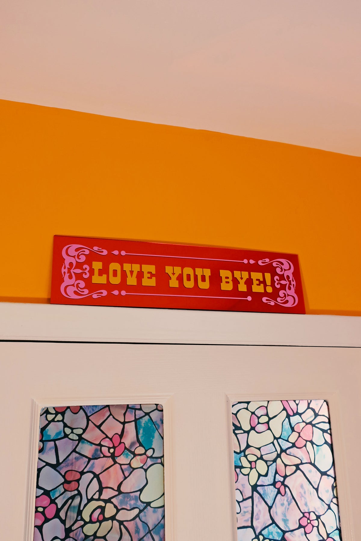 a red sign with the text "I LOVE YOU BYE" written on it, placed above a pair of stained glass windows.