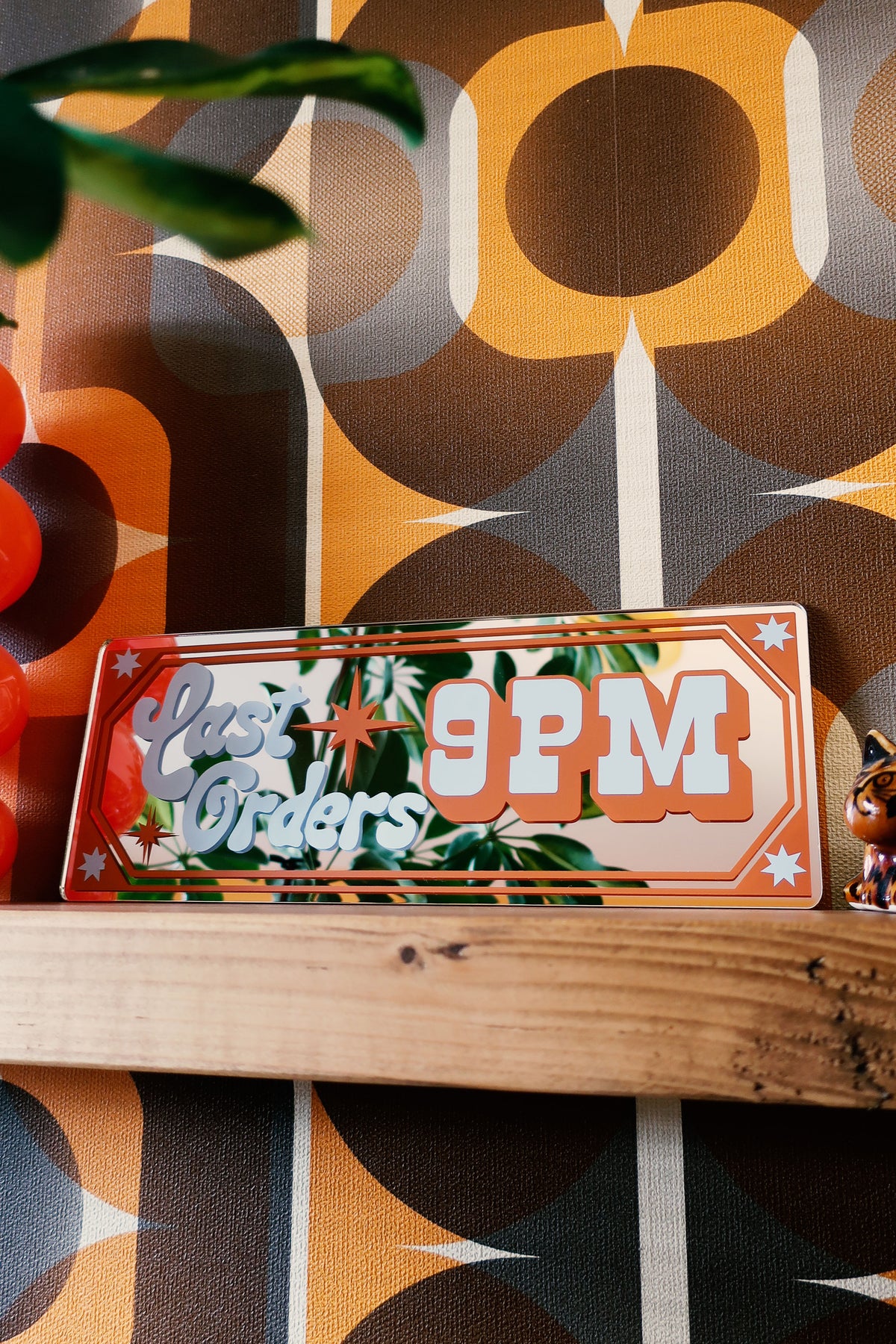 a wooden shelf displaying a sign that reads "Last Orders 9PM", with a colorful, retro-style background.