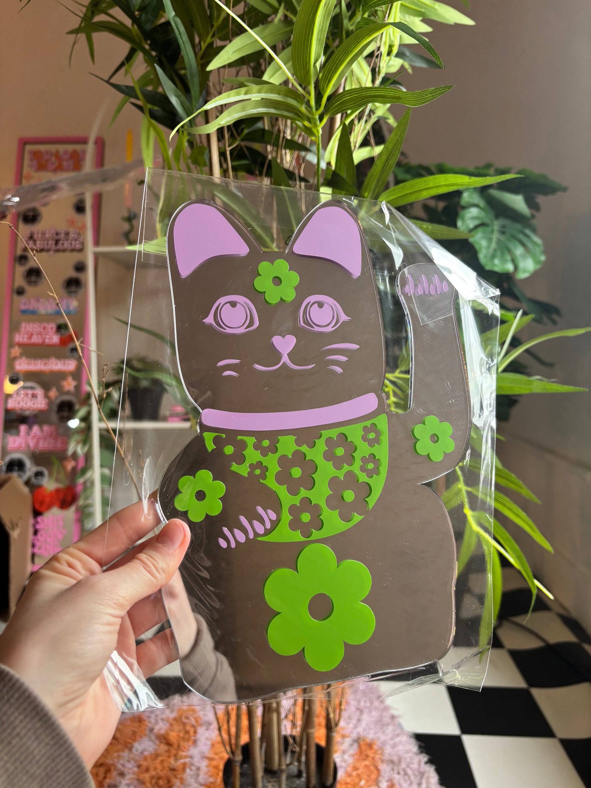 A hand is holding a clear plastic cutout of a cat with a flower design on its chest.
