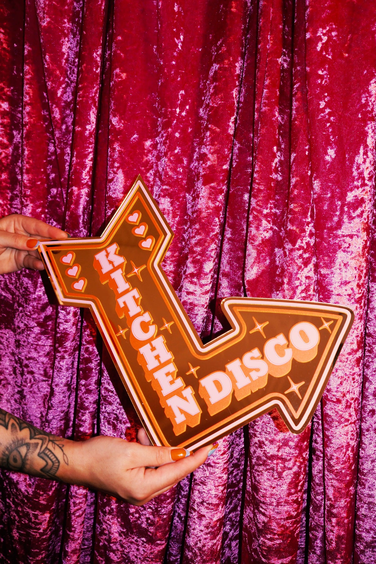 A person's hands holding a large, orange sign with the word "KITCHEN DISCO" written on it.