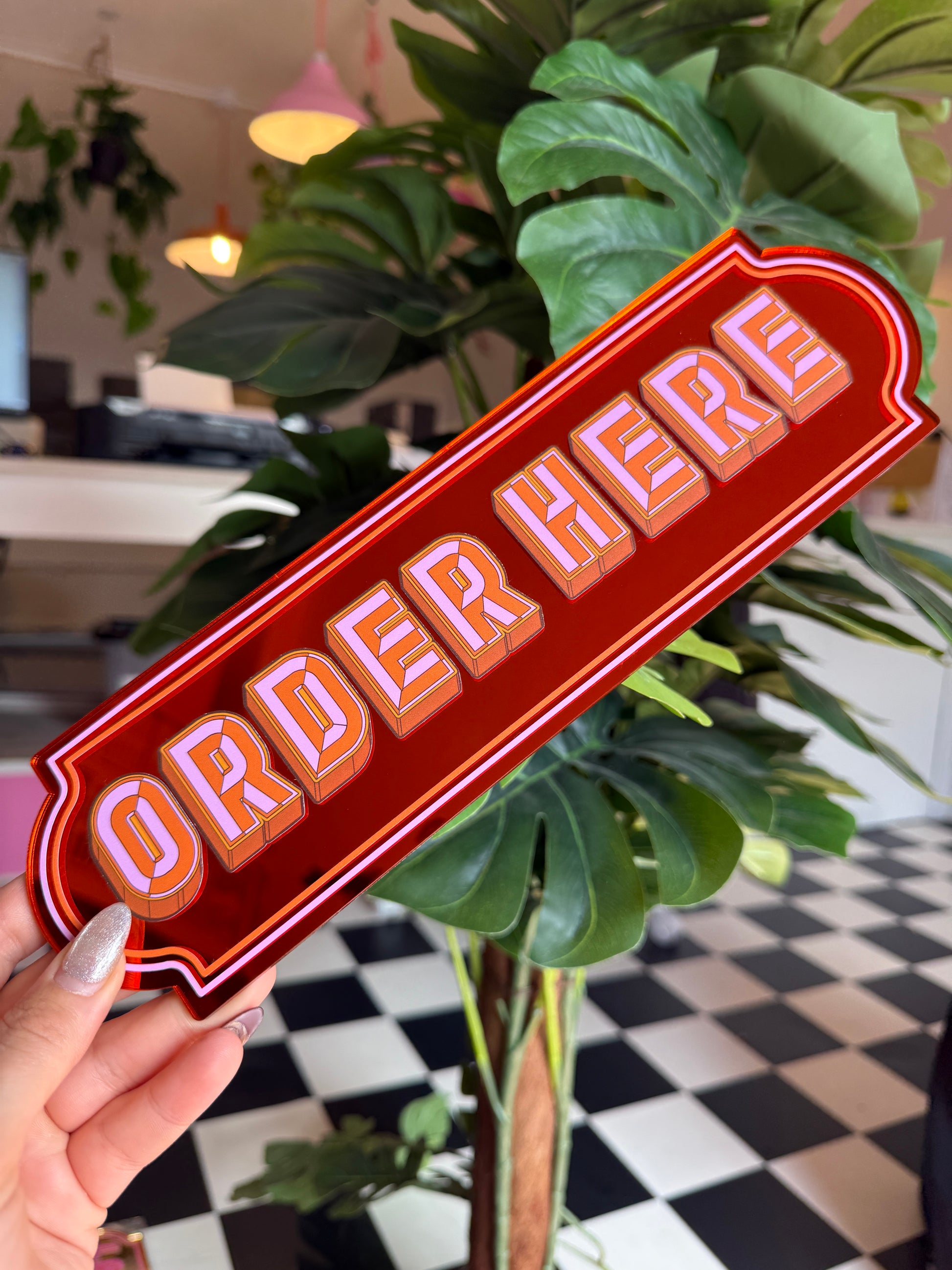A hand holding a red sign with the word "ORANGE" written on it, surrounded by green plants.