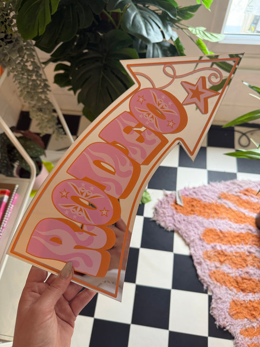 A hand is holding a sign with a pink and orange design, featuring a star and the word "POP" written on it.