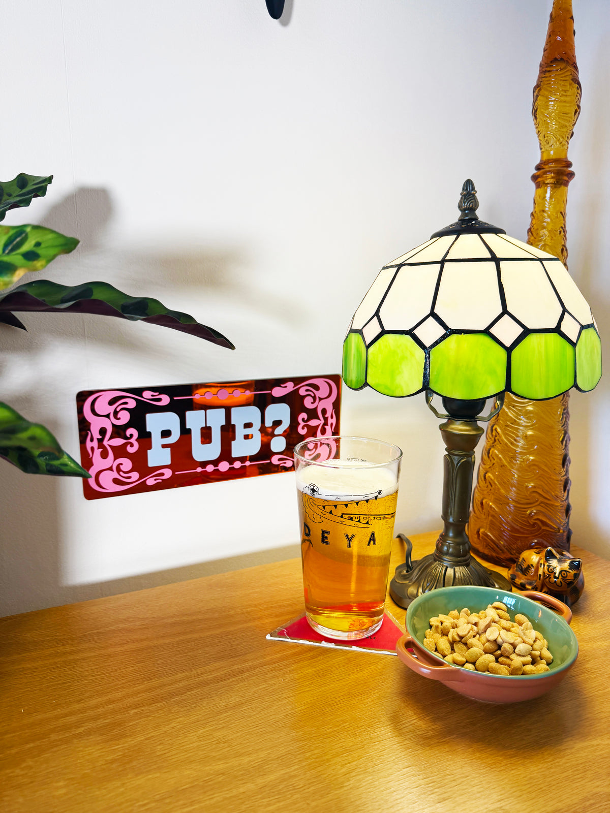 a table with a glass of beer, a bowl of peanuts, and a lamp, along with a sign that reads "PUB?".