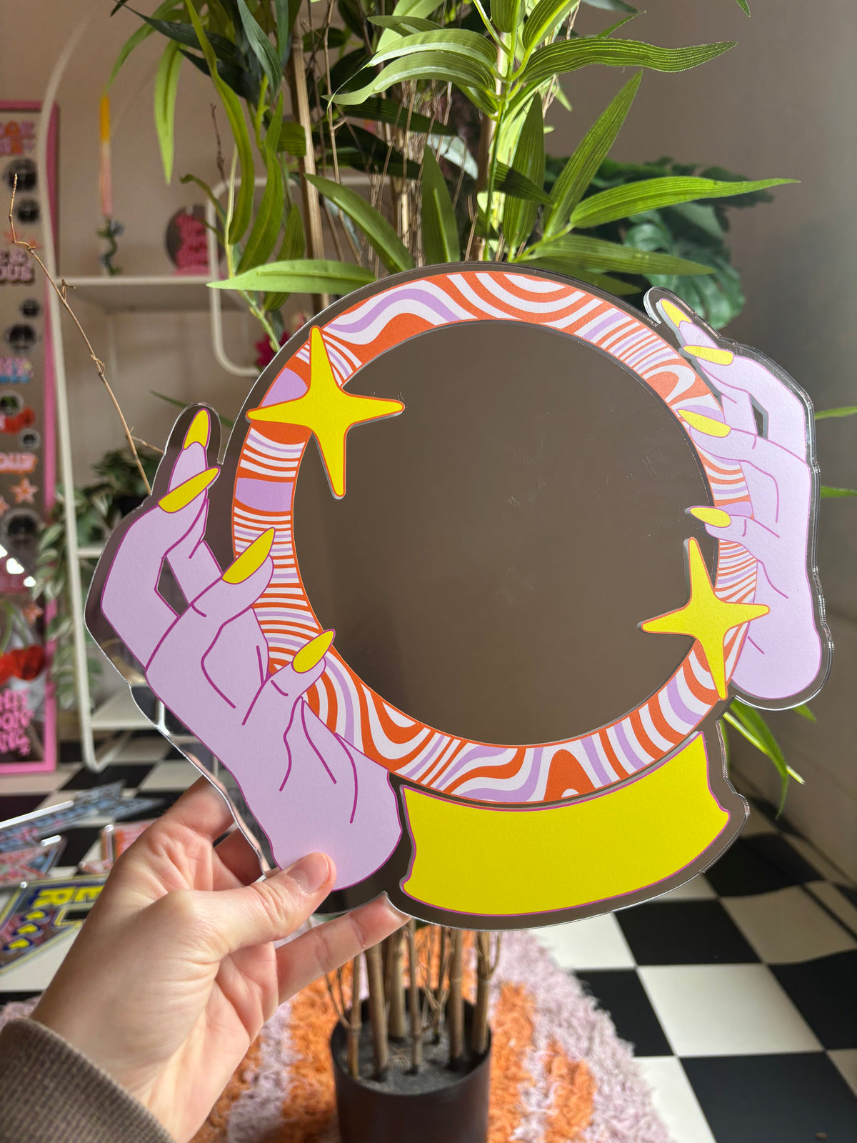 A hand holding a colorful, abstract mirror with a star design.