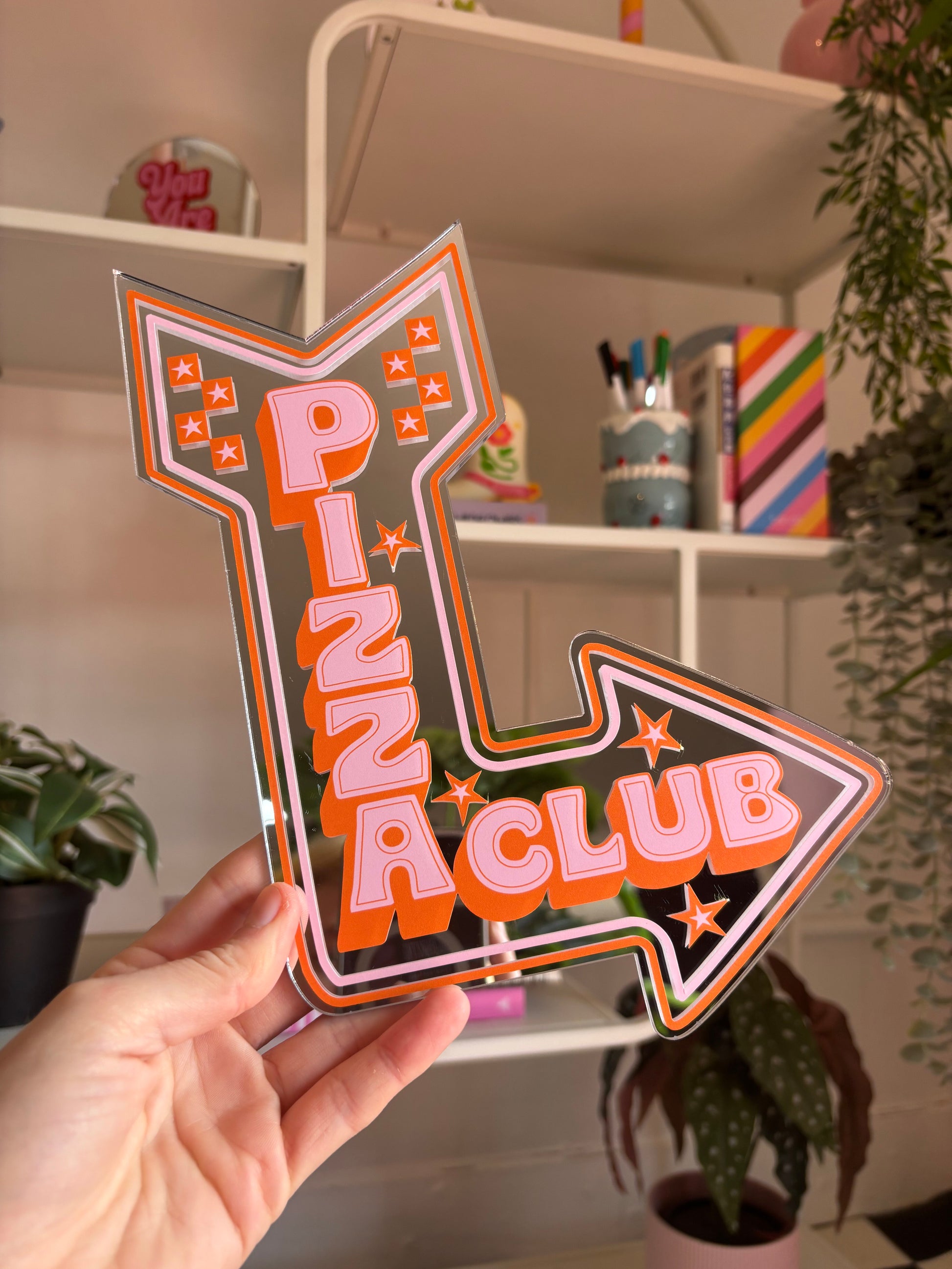 A hand is holding a large sign that says "PIZZA CLUB" in a stylized font, with an arrow pointing to the right.