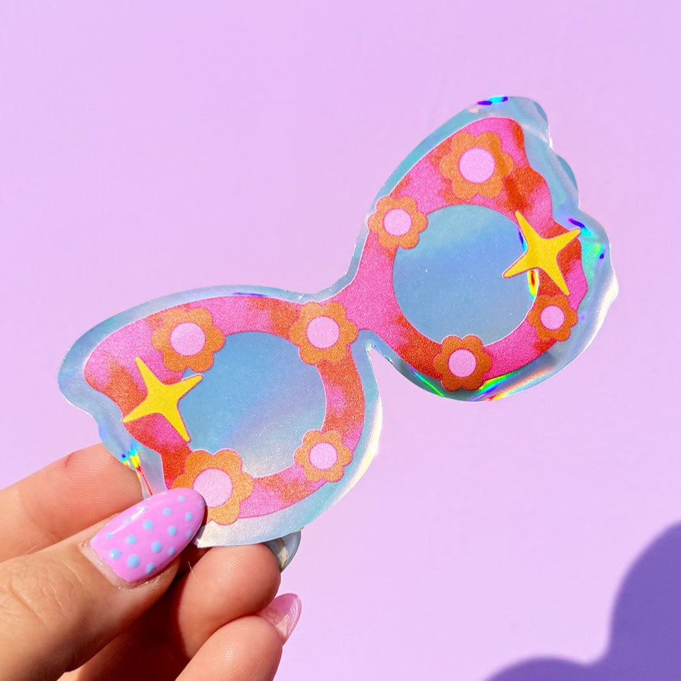 Colorful sunglasses held by a hand against a purple background