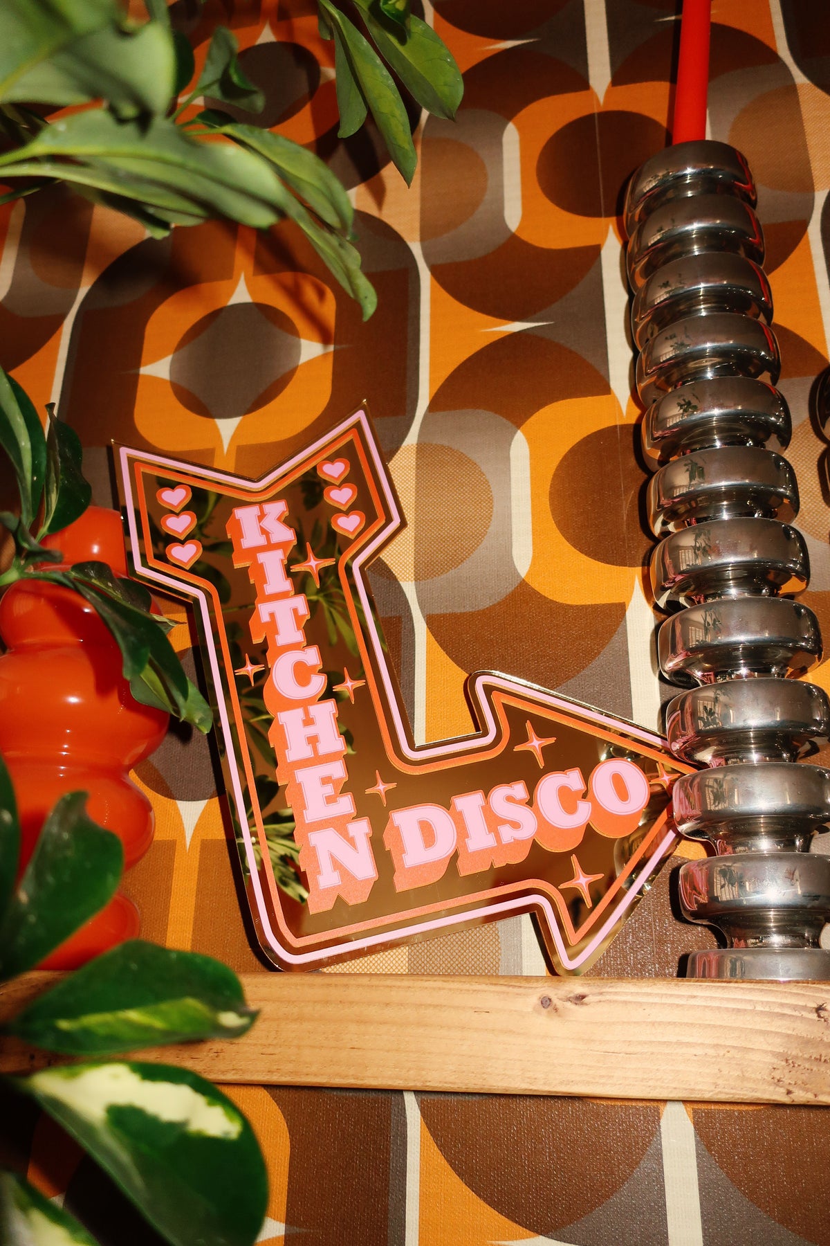 a neon sign that says "KITCHEN DISCO" in a vibrant pink and orange color scheme, placed on a wooden surface.
