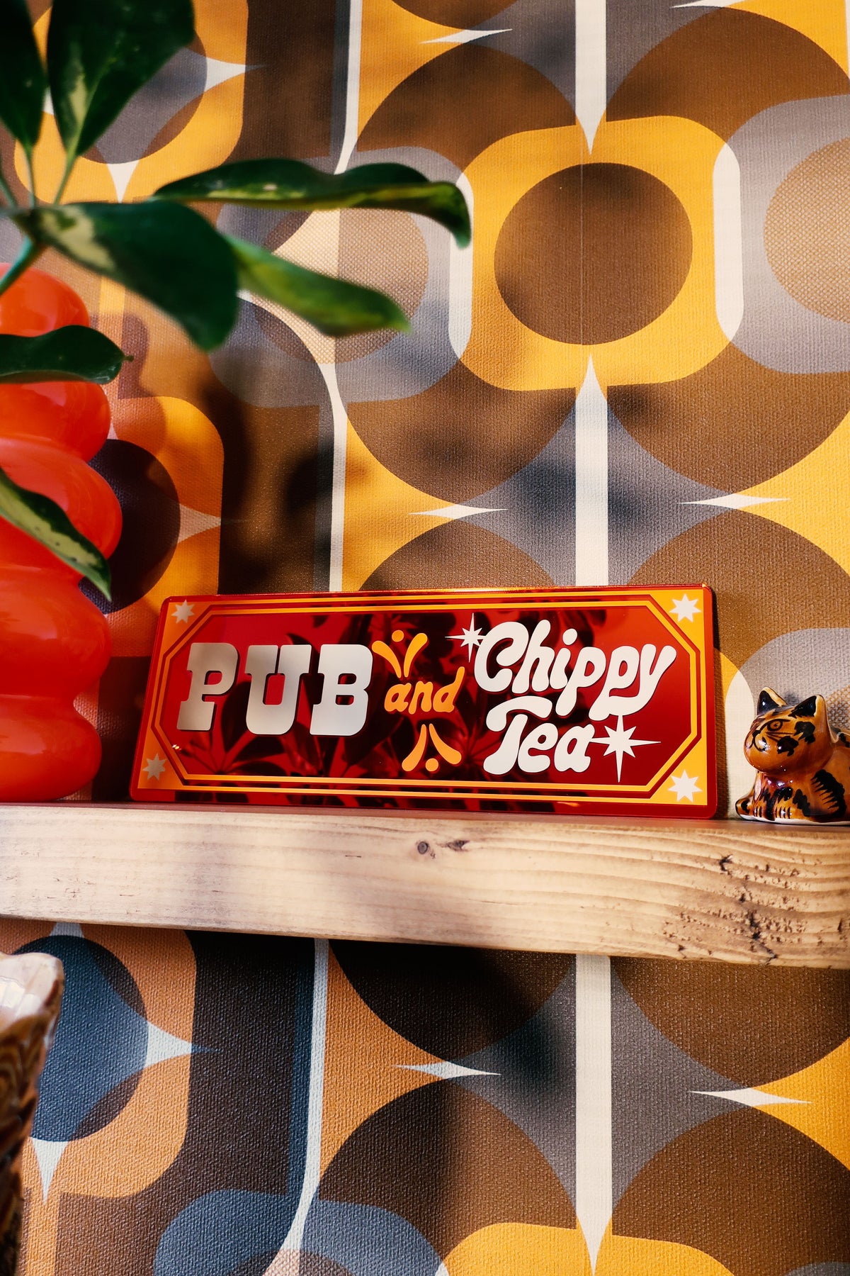 a wooden shelf with a red sign that reads "Pub and Chippy Tea", and a small cat figurine is placed next to the sign.