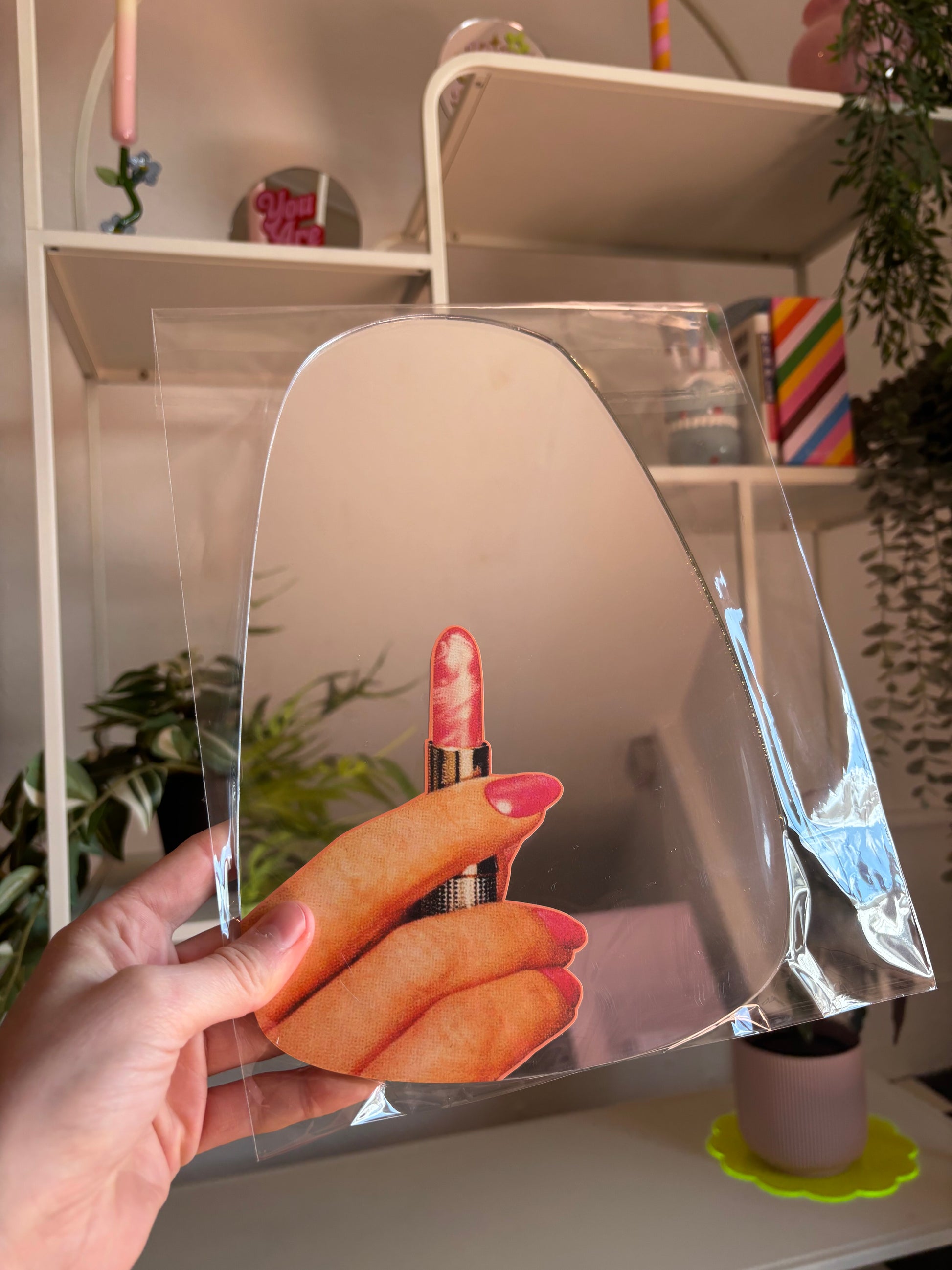 A hand is holding a clear plastic sheet with a hand holding a red lipstick image on it.