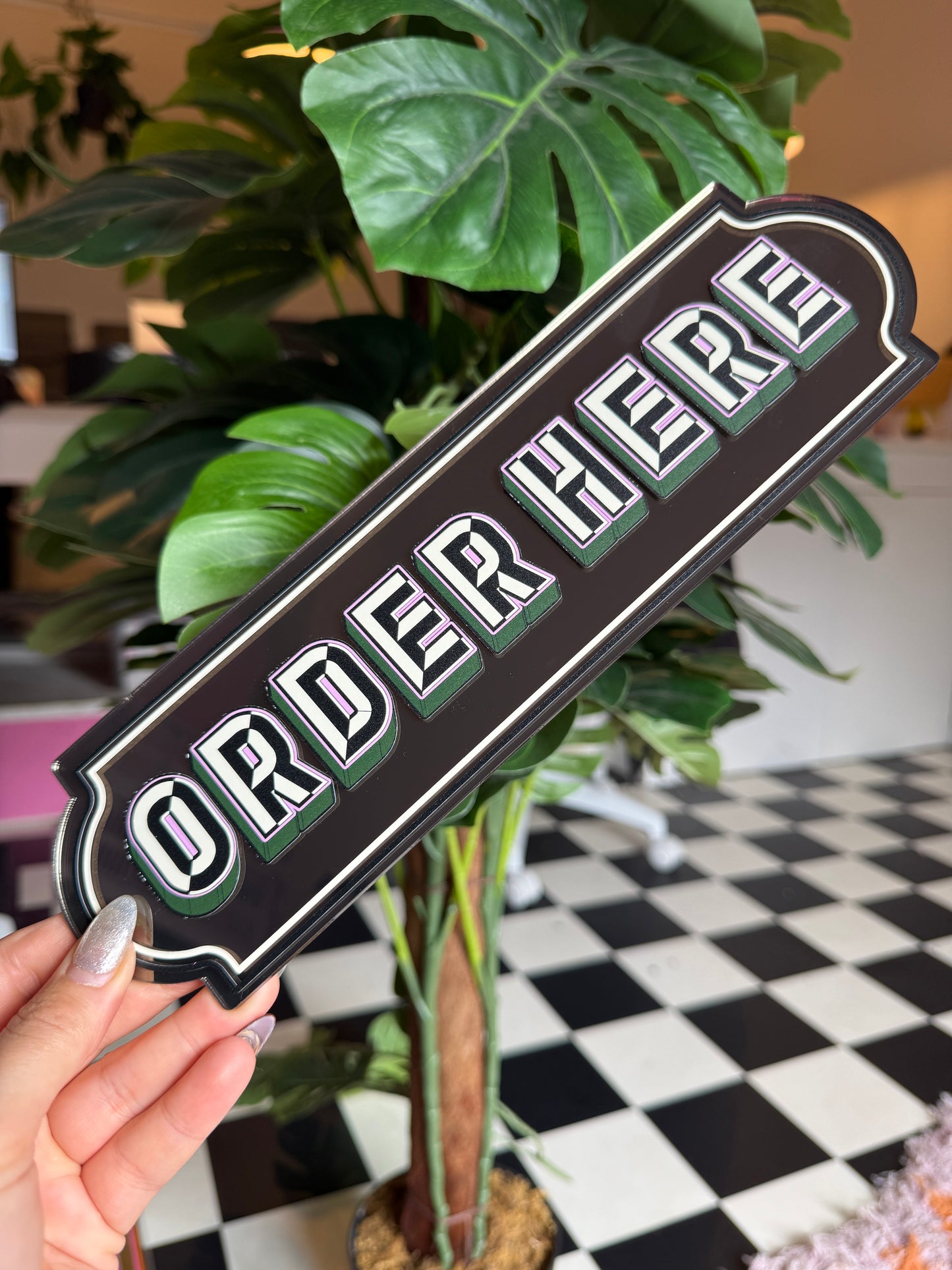 A person is holding a sign with the word "ORDER" on it, surrounded by various potted plants.