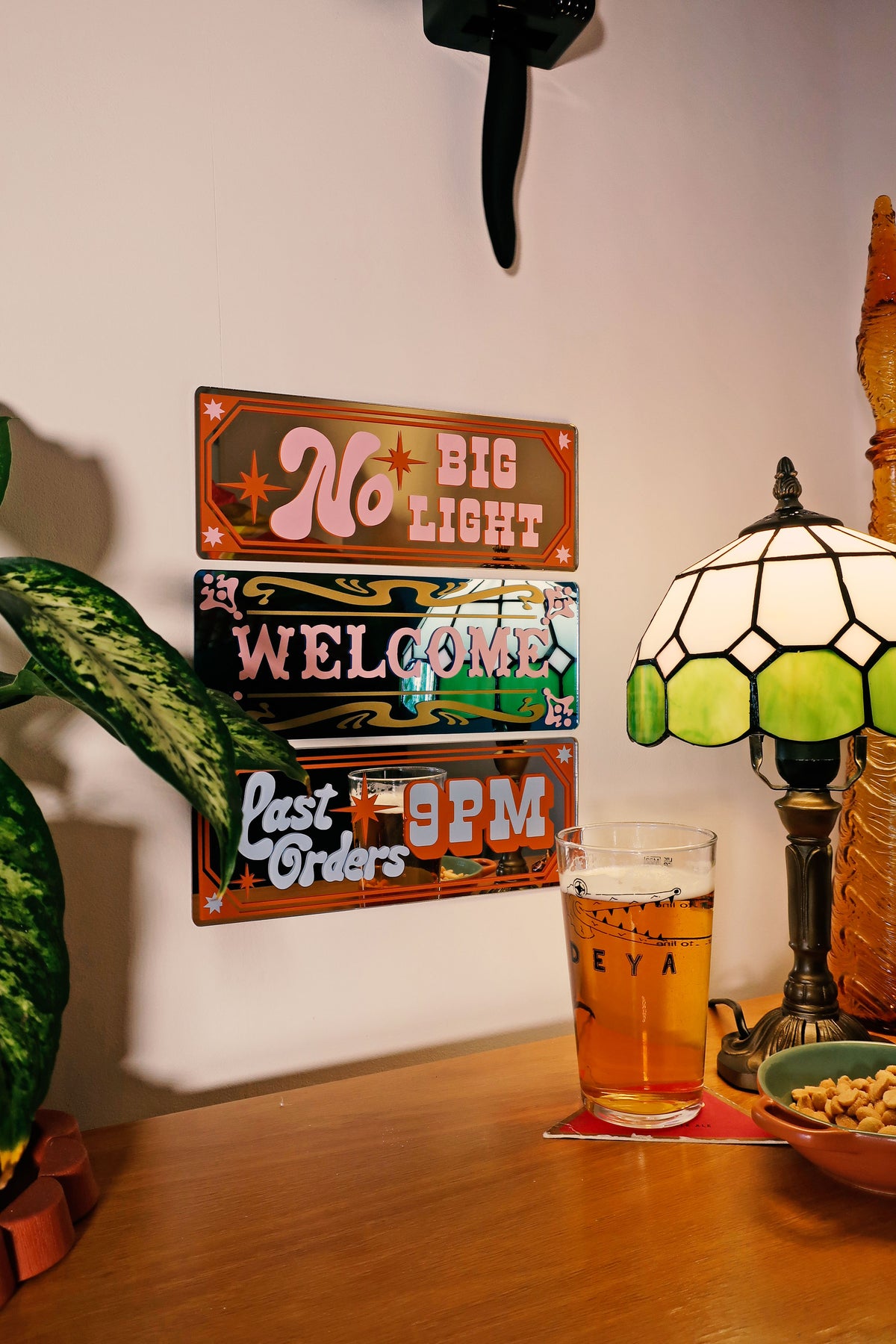 a wooden table with a glass of beer, a lamp, and a sign that reads "No Big Light Welcome".