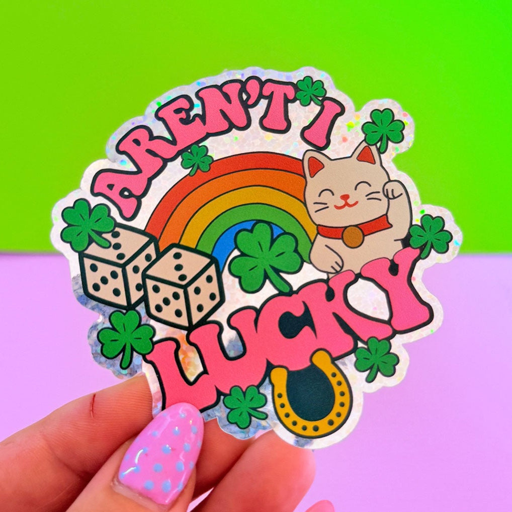 Sticker with a cat, rainbow, and text 'Aren't I Lucky?' held by a hand against a colorful background.