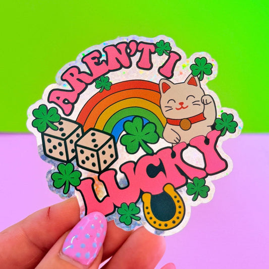 Sticker with a cat, rainbow, and text 'Aren't I Lucky?' held by a hand against a colorful background.