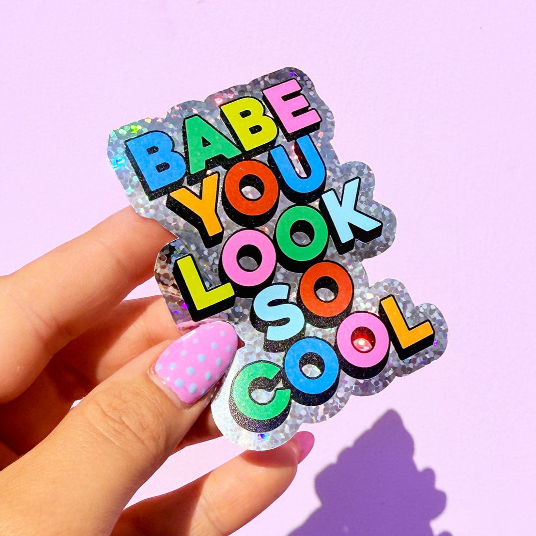Hand holding a colorful sticker with text against a light purple background