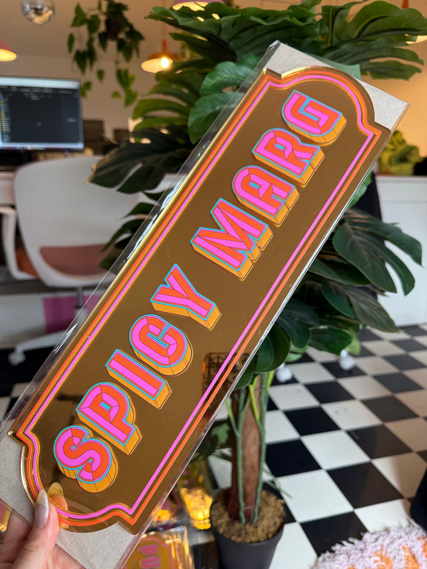 a person holding a sign with the word "SPIDERS" written on it, surrounded by various plants and a checkered floor.