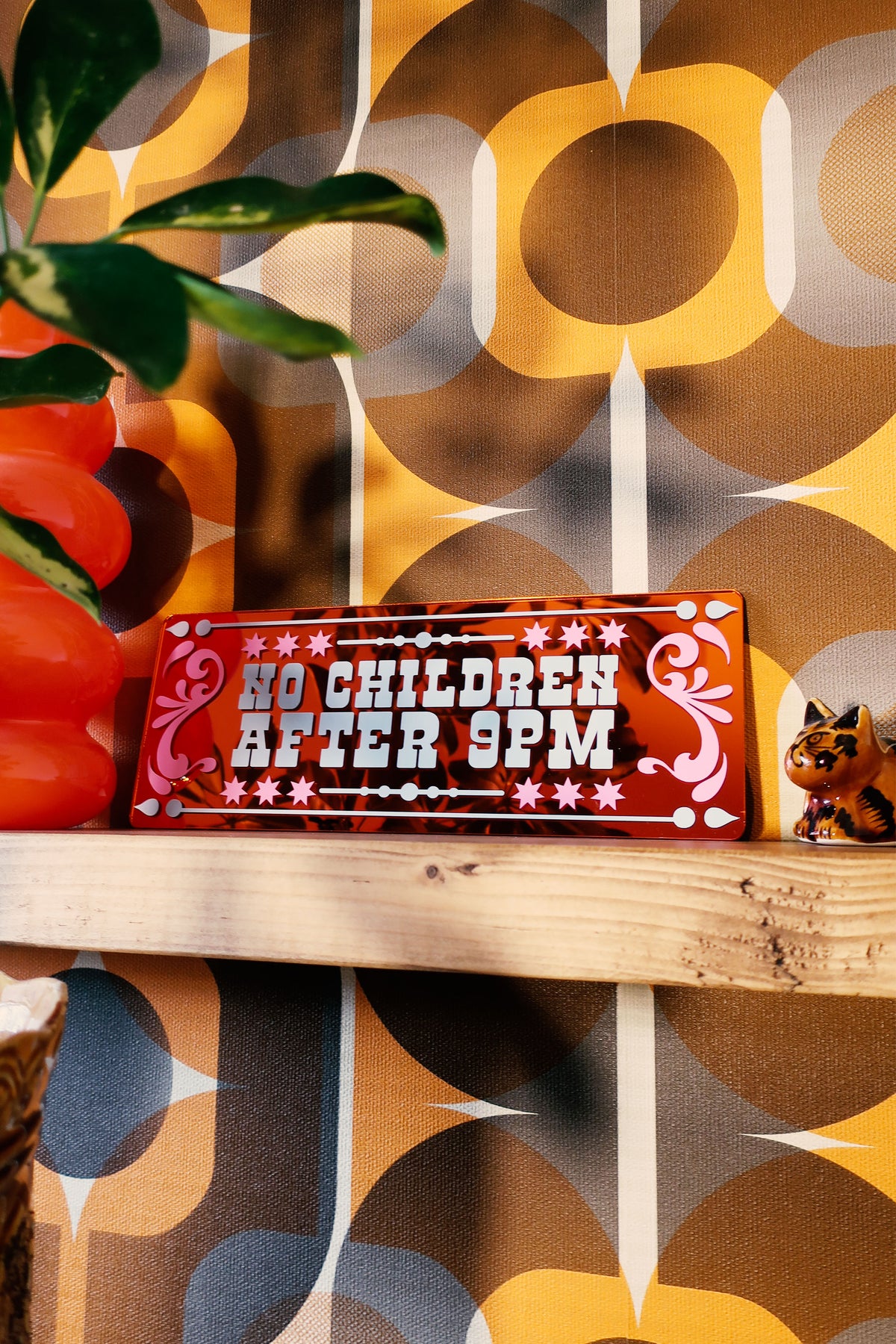 a wooden shelf with a red sign that reads "No Children After 9PM" and a small cat figurine.
